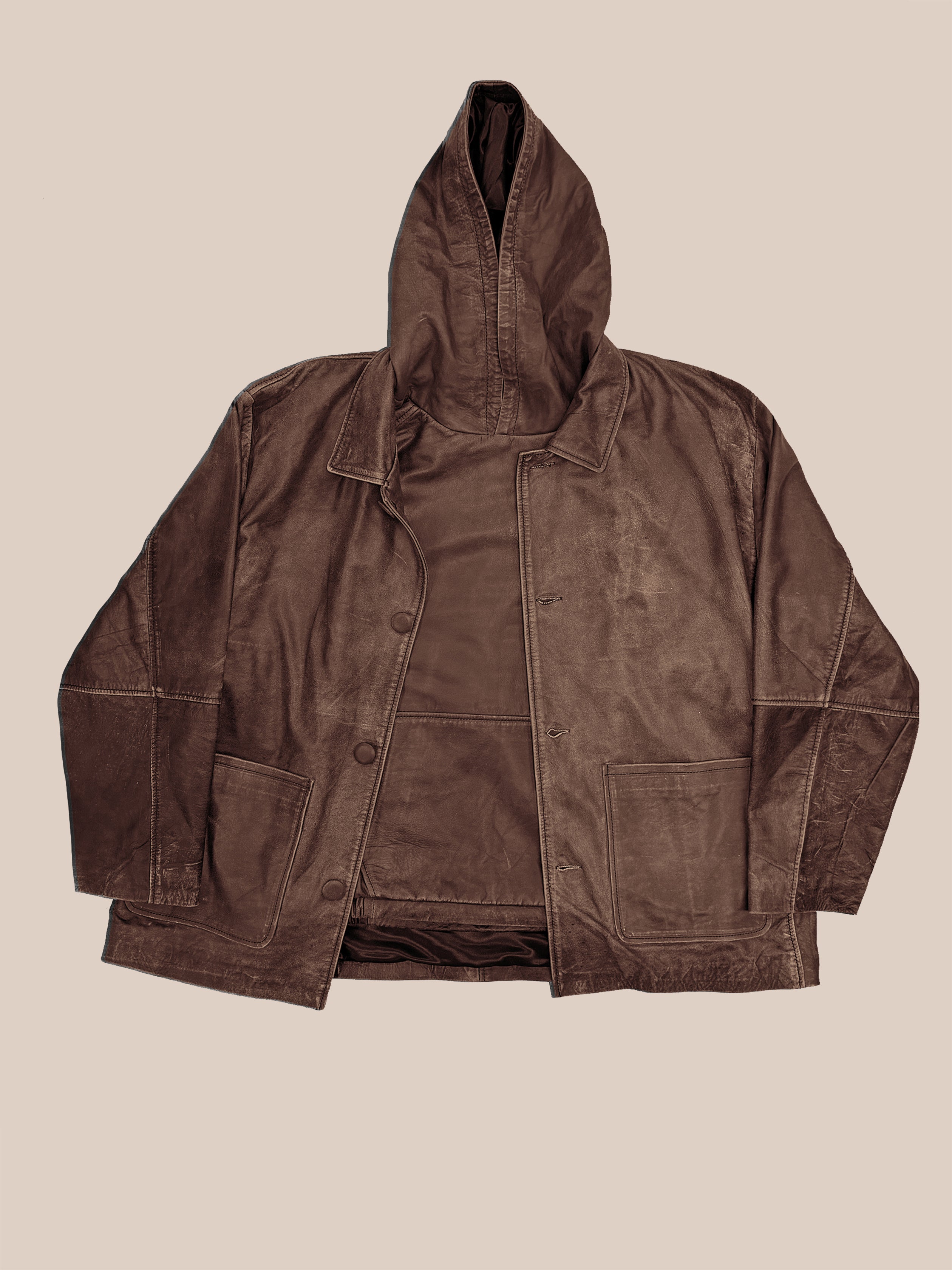 The FOUND Double Layer Leather Hooded Jacket, in brown leather with visible stitching, front buttons, and large pockets, is shown flat on a beige background—a stylish unisex outerwear piece.
