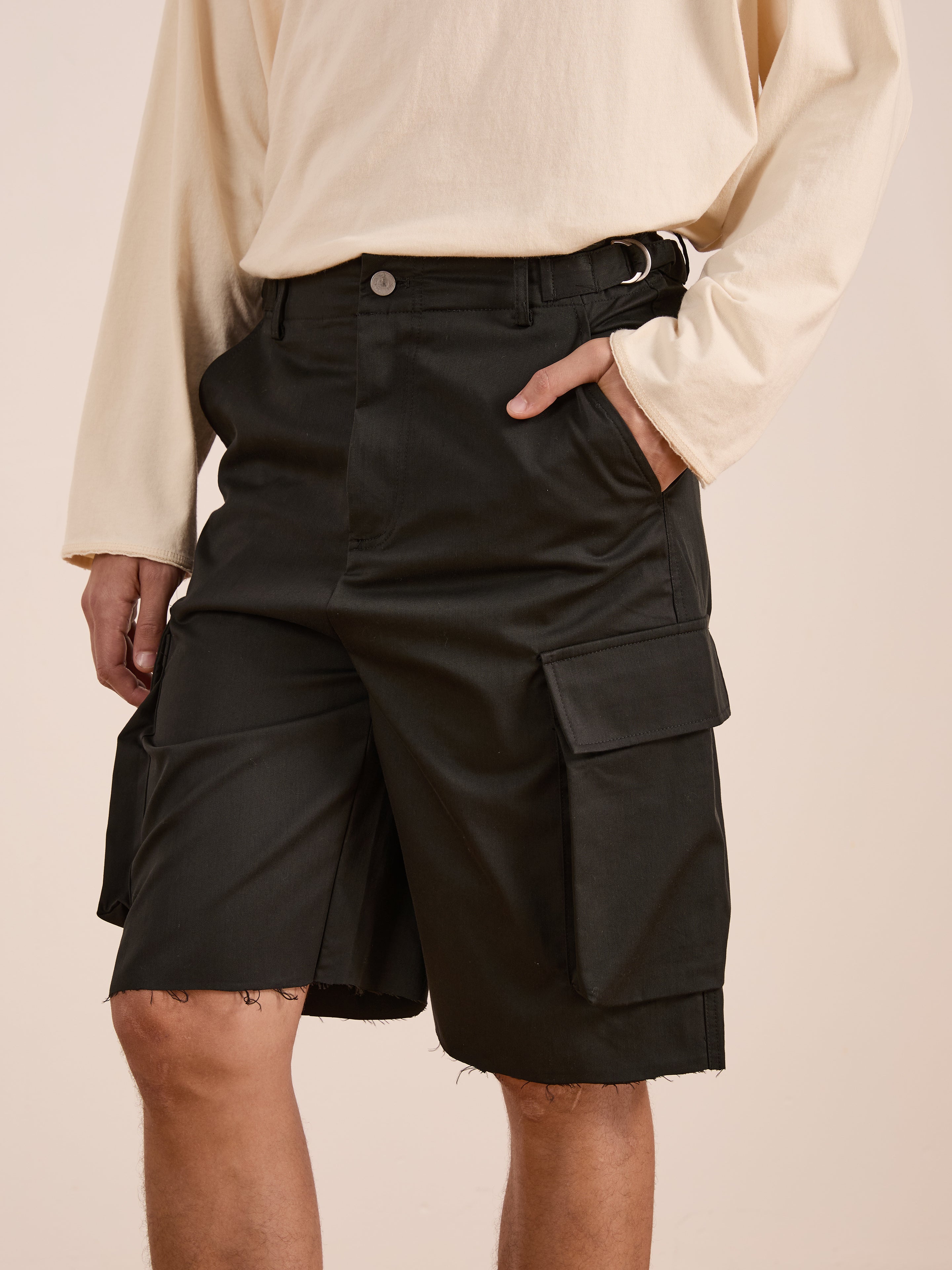 A person in a cream long-sleeve shirt and black Found Elbas Cargo Shorts, featuring dual cargo pockets and adjustable waist tabs, stands with one hand in a pocket.