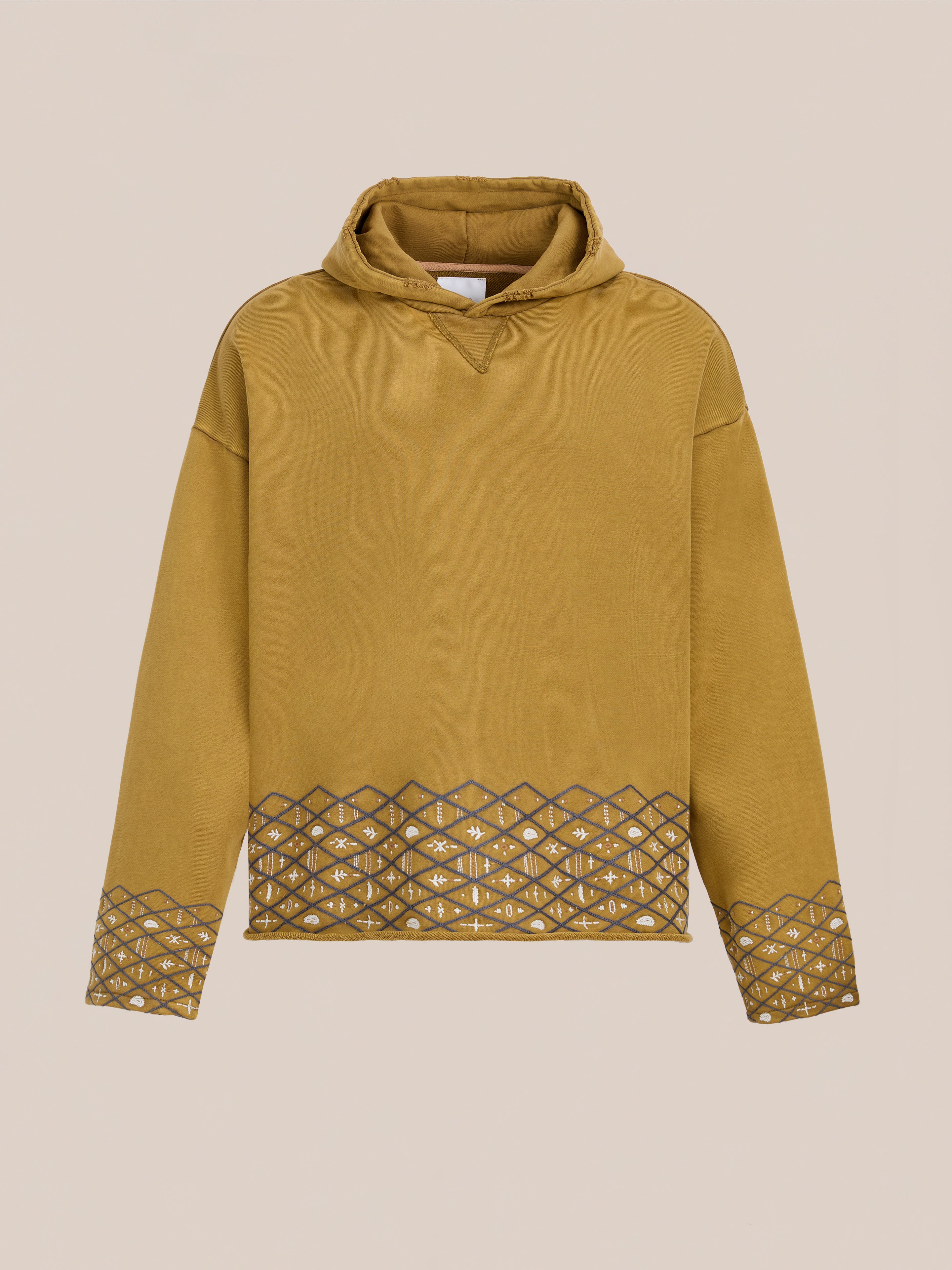 The FOUND Embroidered Border Hoodie is a mustard yellow unisex relaxed fit hoodie featuring geometric cut-out patterns along the hem and sleeves, shown on a plain beige background.