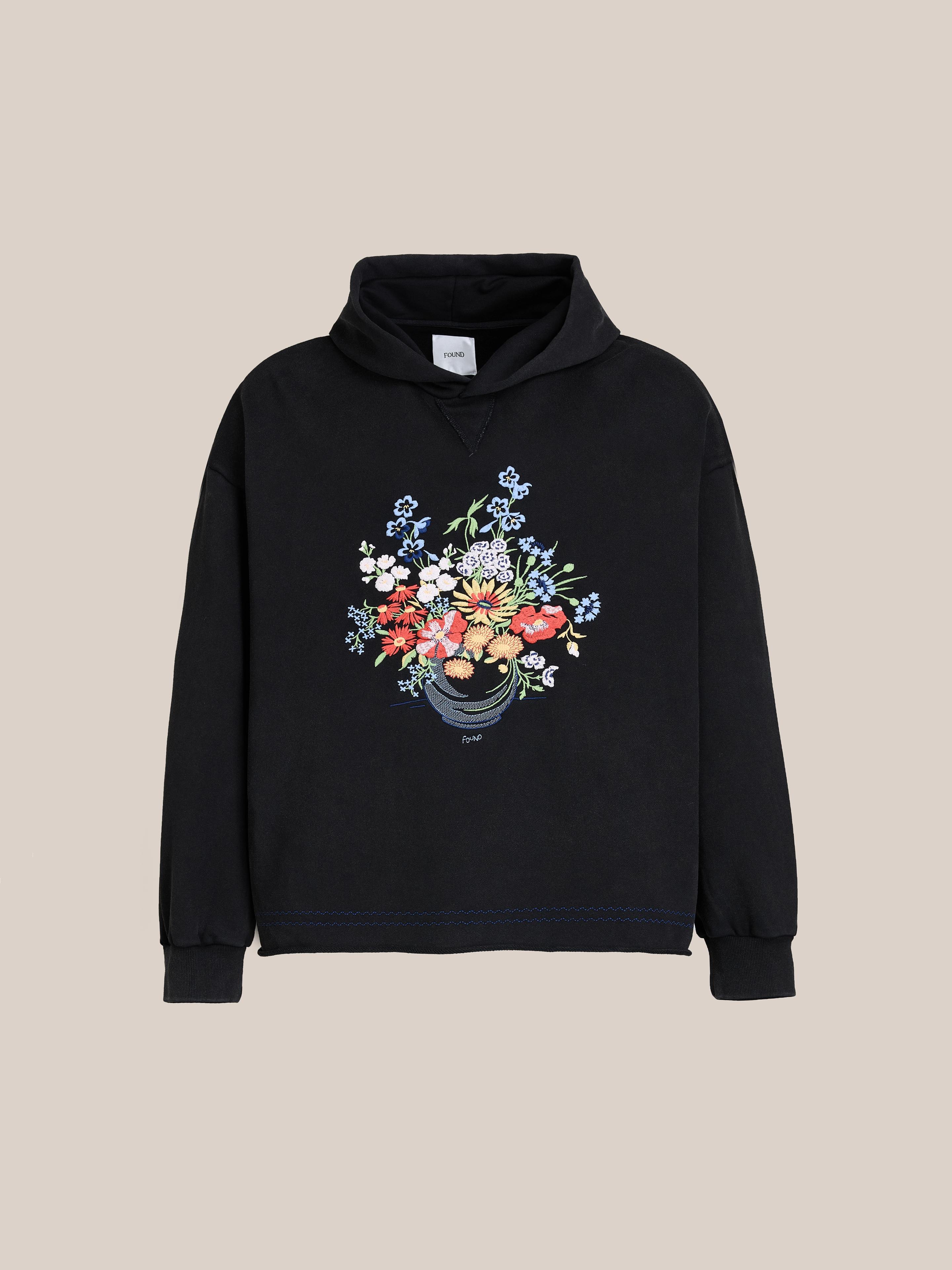 The FOUND Bouquet Flowers Hoodie is black with a vibrant floral bouquet graphic on the front, shown against a plain beige background.