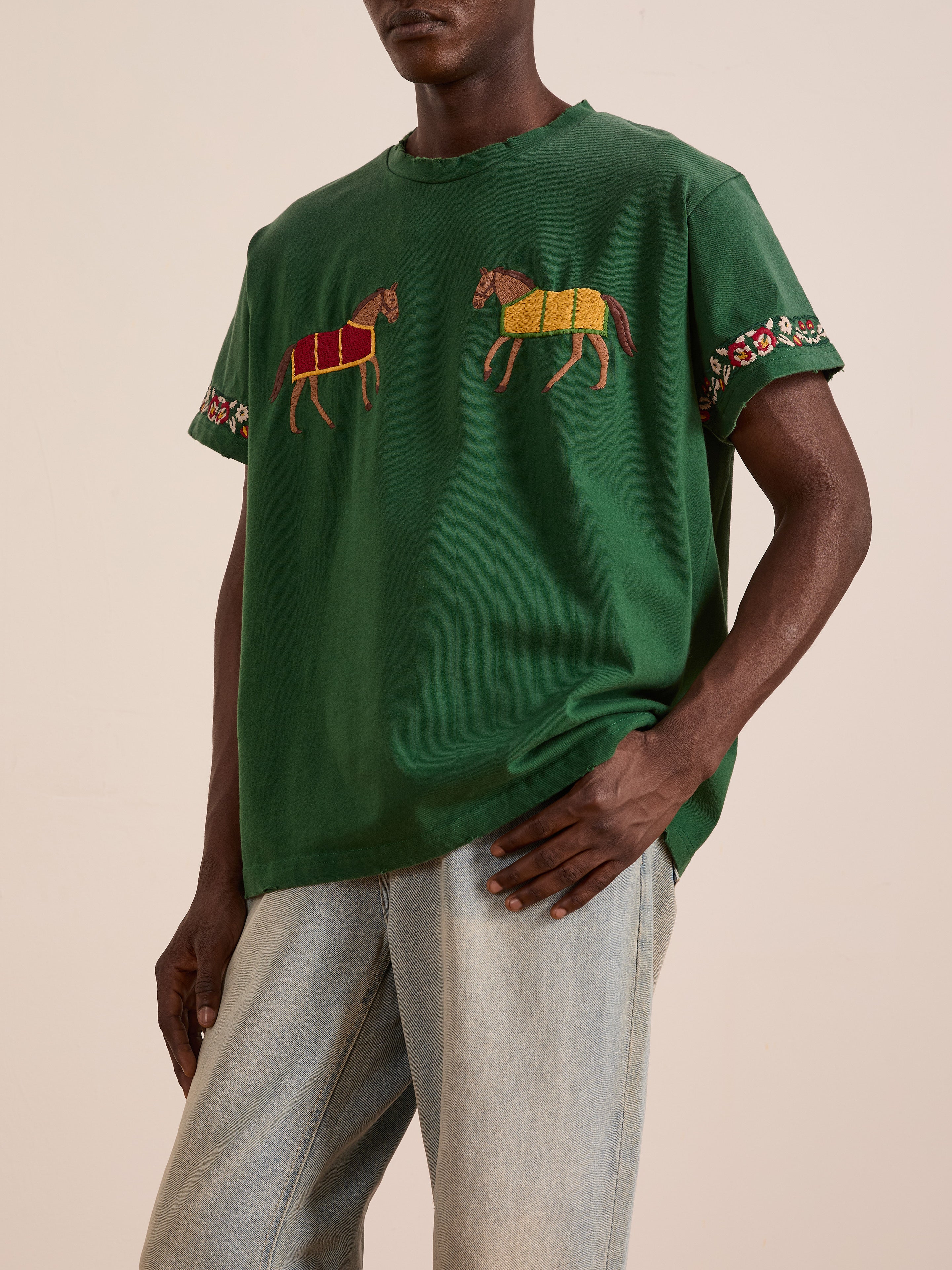 A person wears the FOUND Horse Equine Tee featuring embroidered horses and floral sleeve patterns, paired with light blue jeans.