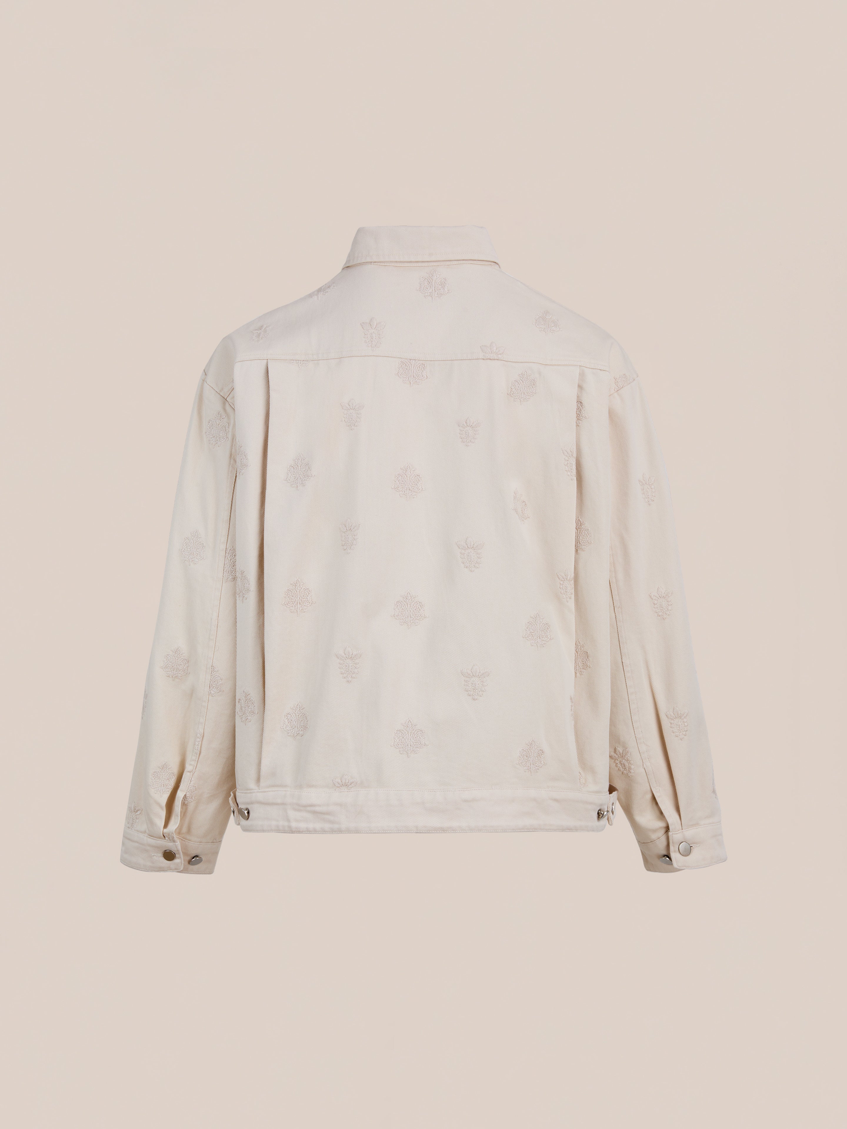The Found Embroidered Motif Jacket is a cream-colored unisex piece shown from the back, featuring a subtle embroidered pattern and buttoned cuffs—a modern twist on the classic chore jacket.