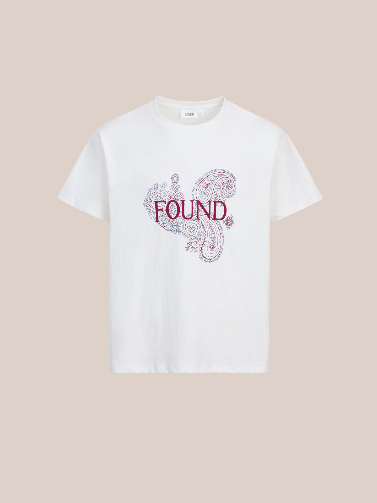 FOUND’s Embroidered Paisley Tee: a white unisex cotton shirt with “FOUND” in red over a decorative bandana paisley, shown on a plain beige background.