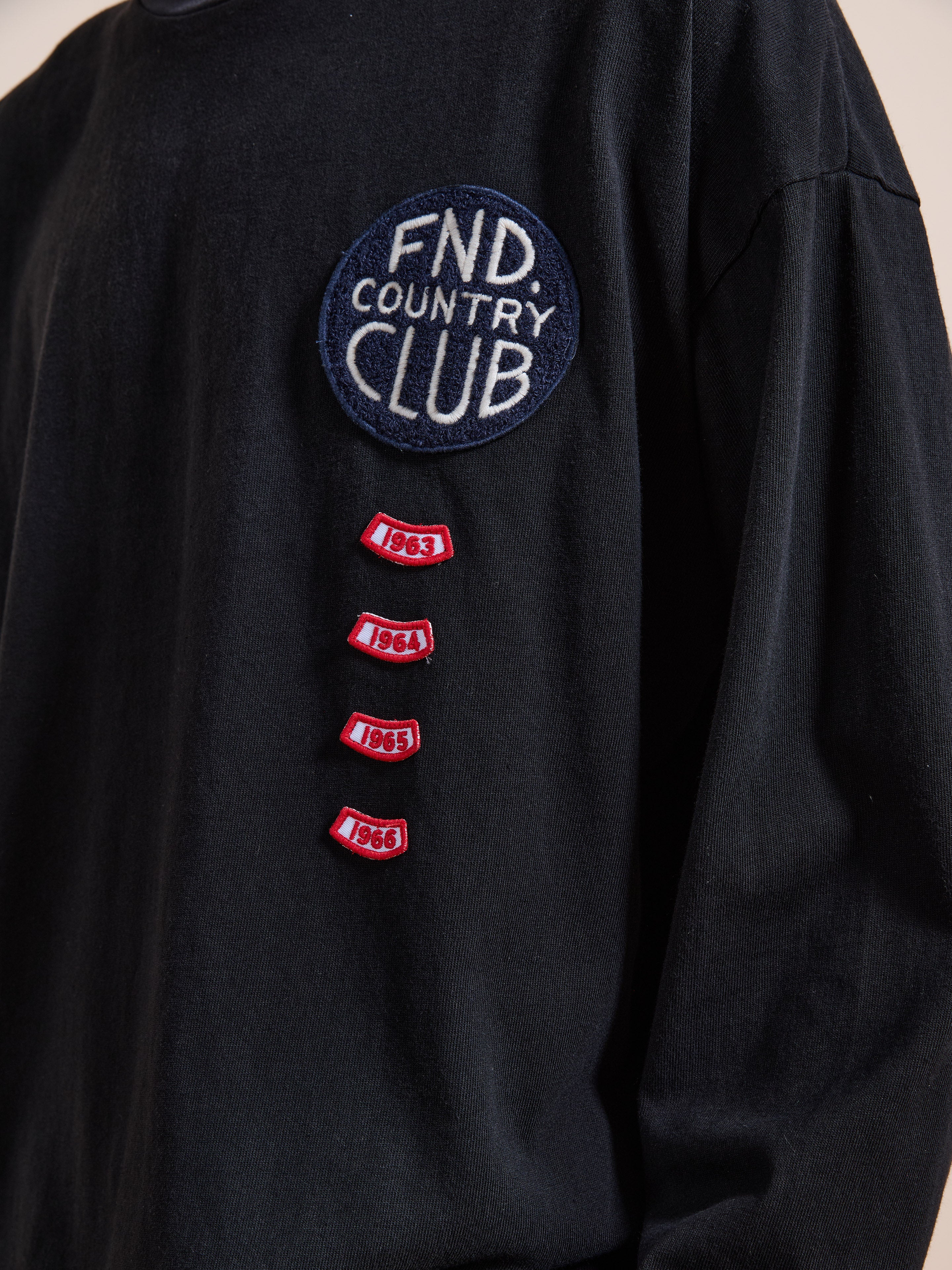 The FOUND Embroidered Patches LS Tee is a vintage washed black shirt with a "FND Country Club" patch and four small red patches below, each embroidered with the years 1963, 1964, 1965, and 1966.