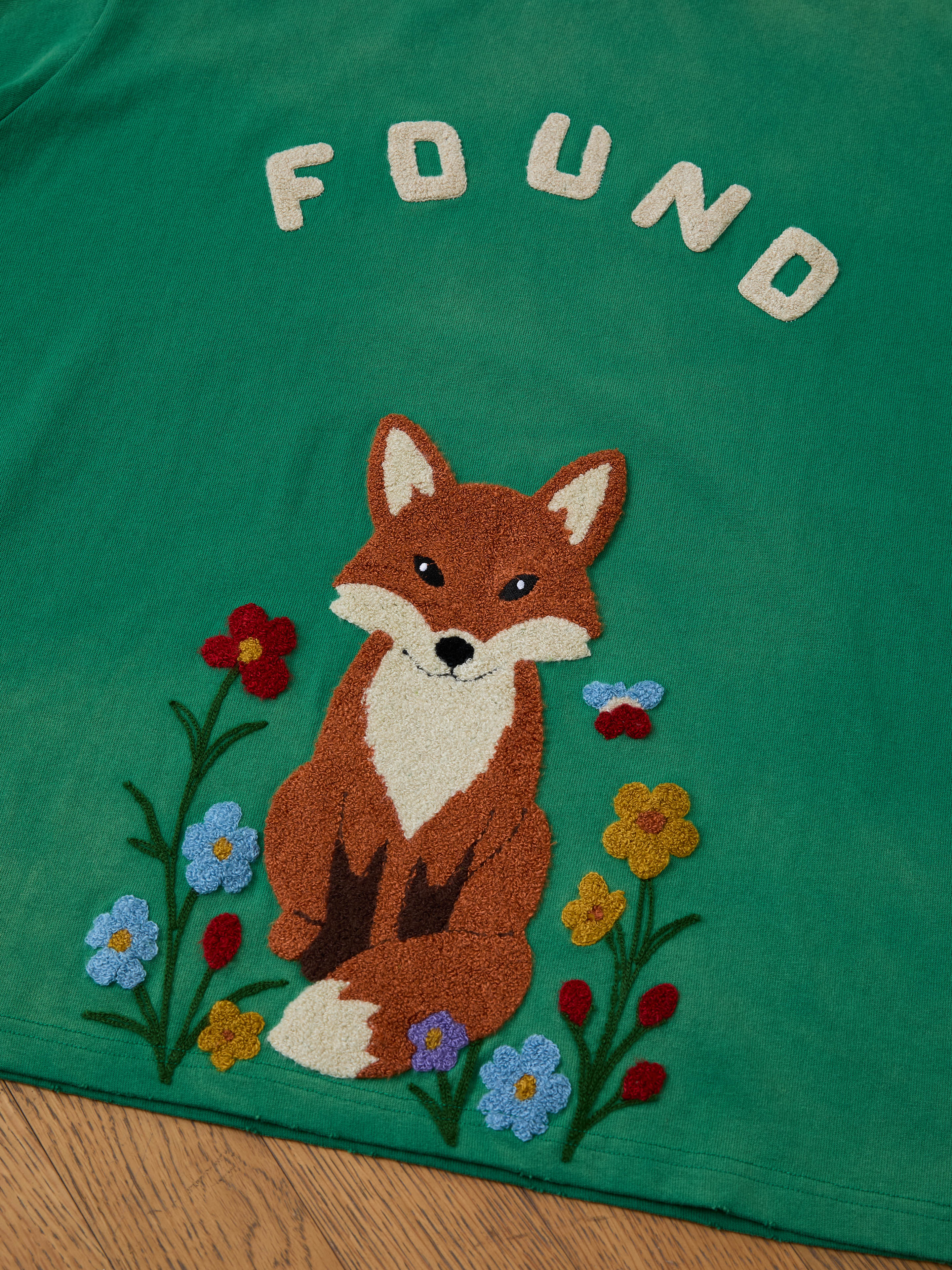 The FOUND Embroidered Wildlife Tee features a green vintage wash and an embroidered fox among colorful flowers—perfect for nature lovers.