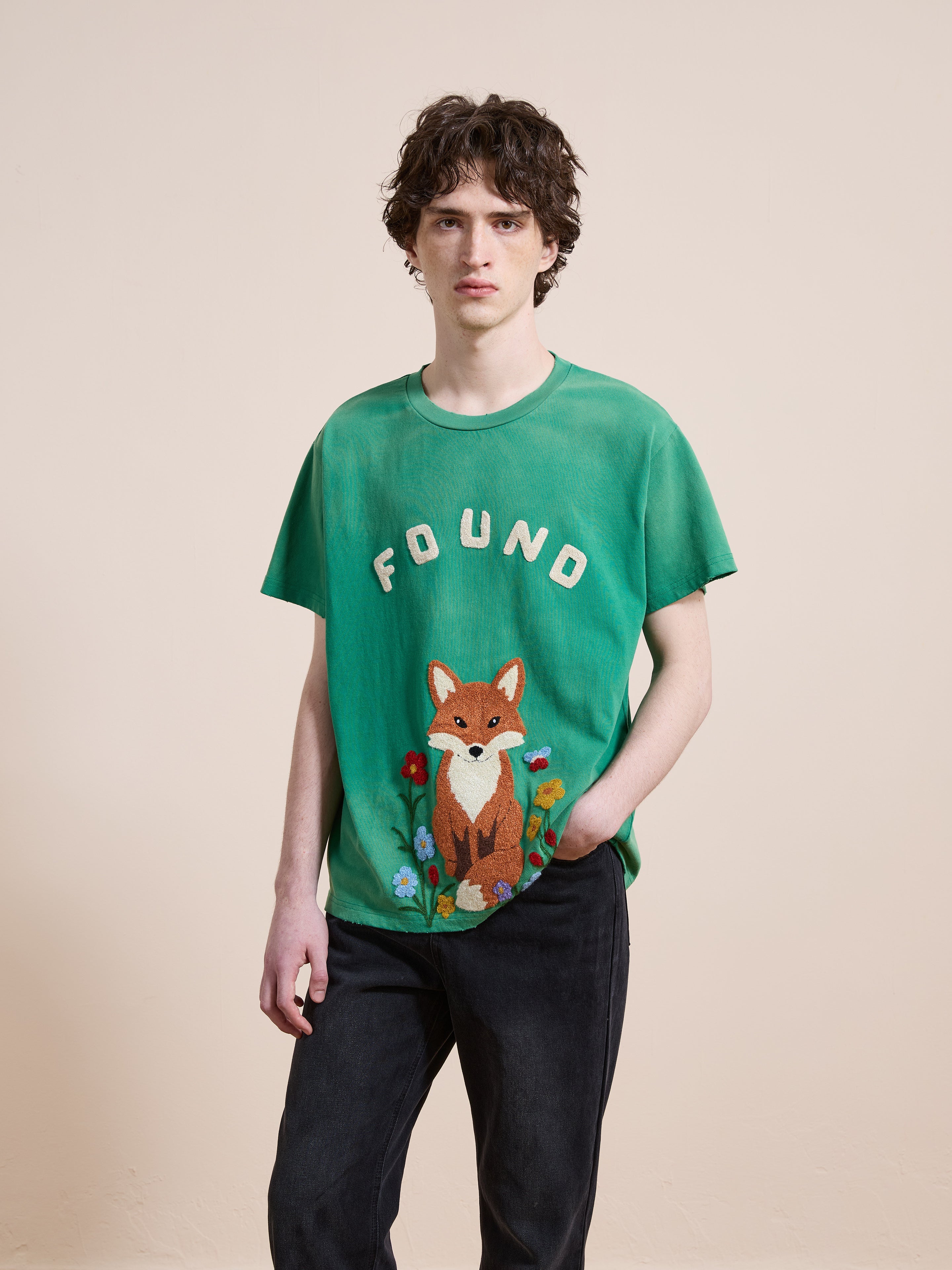 Someone wears the FOUND Embroidered Wildlife Tee, featuring "FOUND" above an embroidered fox and flowers, standing against a plain light background.
