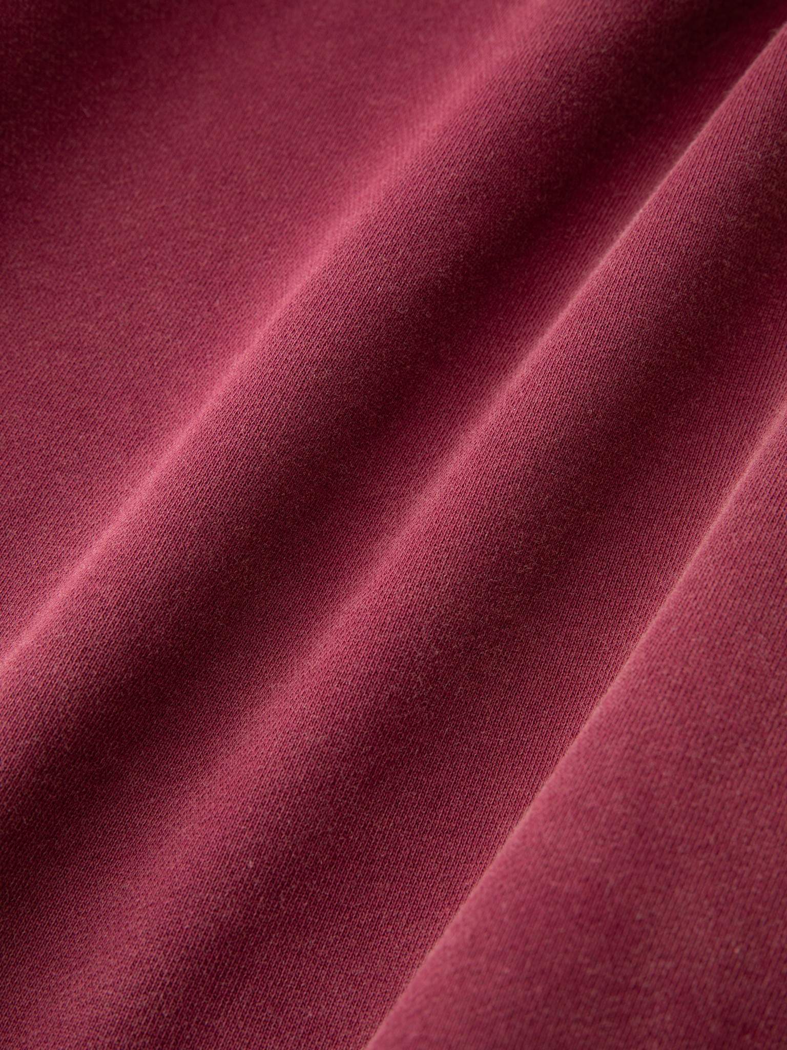 Close-up view of maroon fabric with visible diagonal folds, showcasing a soft, smooth texture that evokes the comfort of the FOUND Embroidered Wildlife Hoodie.