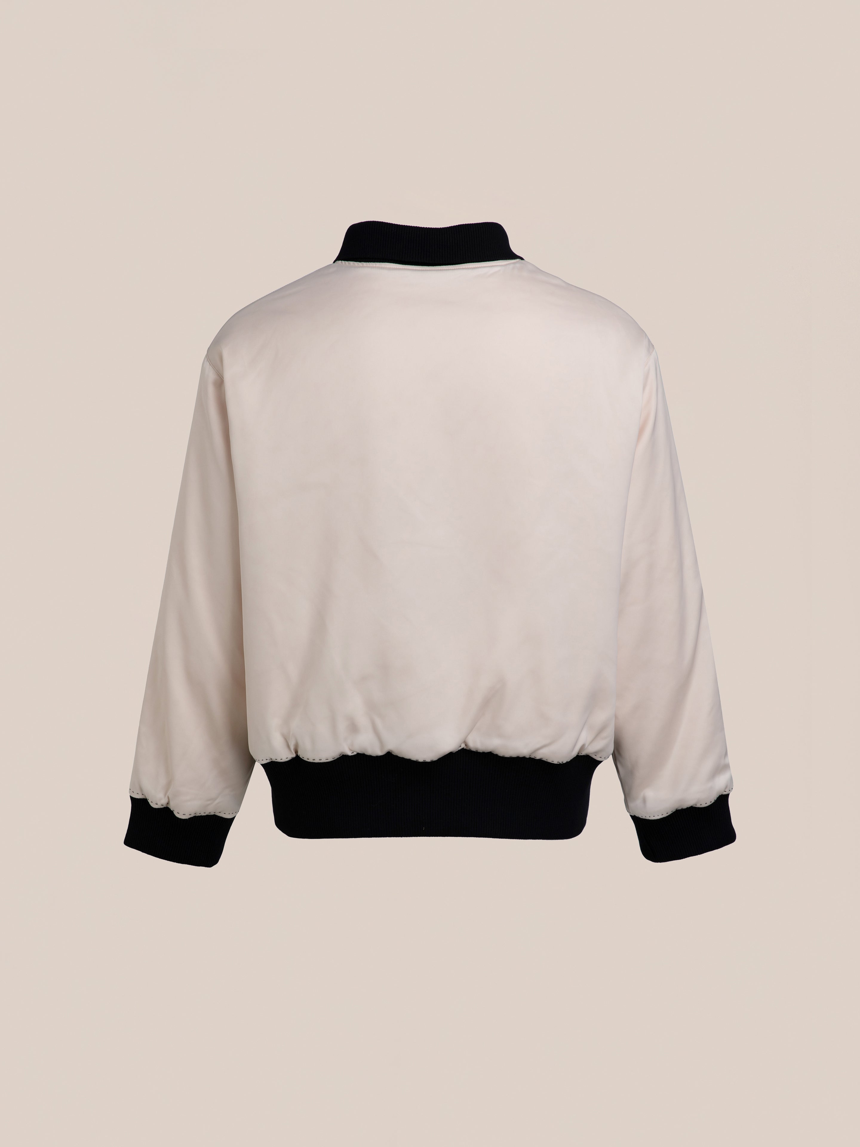 Back view of the FOUND Daman Satin Jacket, featuring a light-colored design with a black collar, cuffs, and waistband against a plain, beige background.