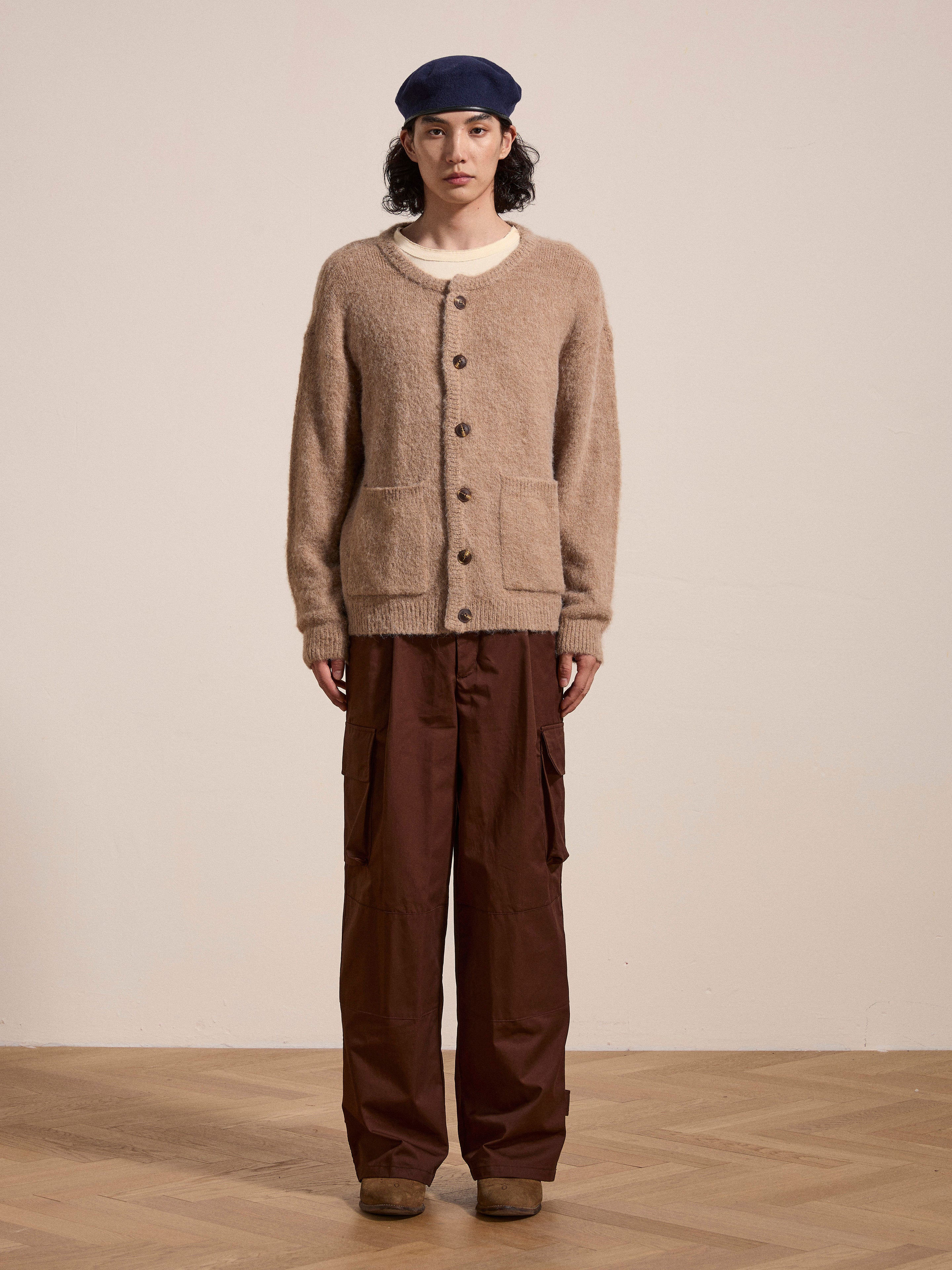 A person wearing the FOUND Mohair Cardigan in beige with tortoise buttons, a white shirt, brown cargo pants, brown shoes, and a blue beret stands against a plain background.