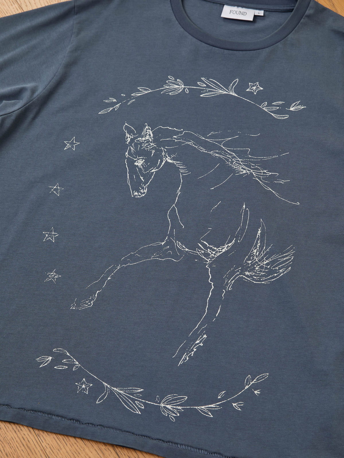 The Faded Horse Trot Tee by FOUND is a unisex, relaxed fit shirt with a white horse, stars, and leafy branches graphic on the front.