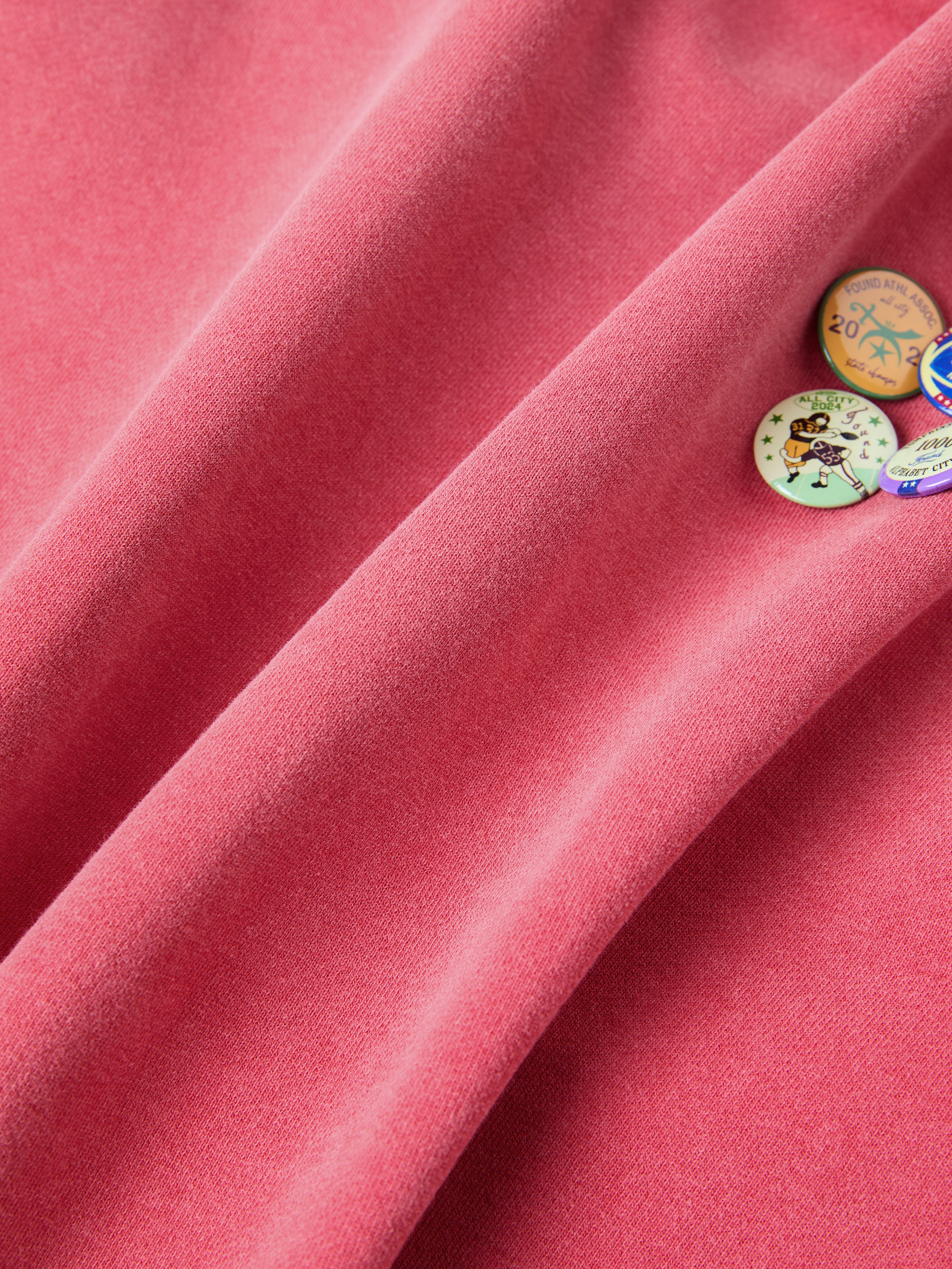 Close-up of a pink fabric with colorful, vintage-inspired pins attached, showcasing the FOUND brand's Multi Patch Hoodie.
