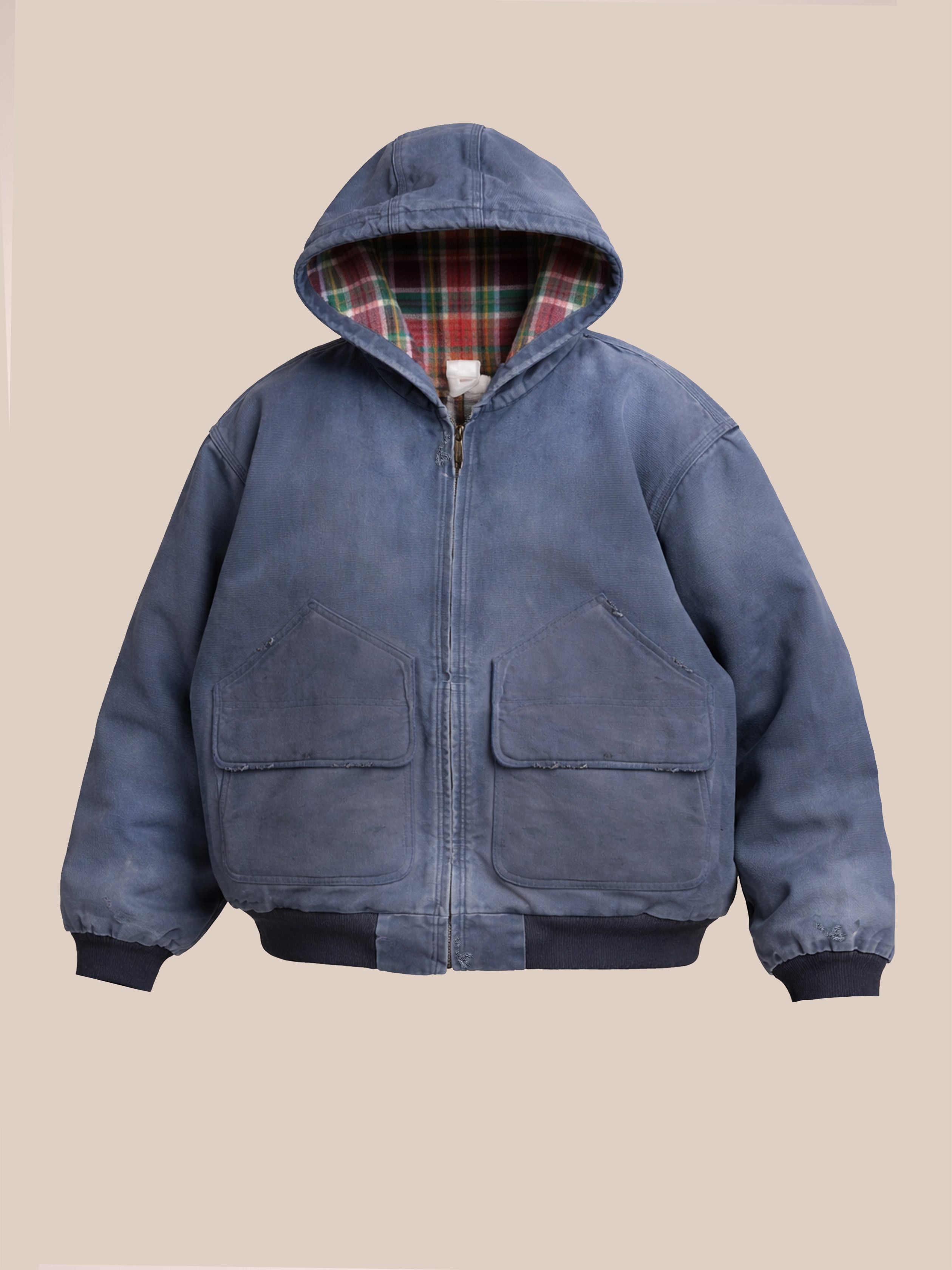 The FOUND Faded Canvas Work Hoodie features a blue plaid flannel lining, front pockets, and is shown on a plain beige background.
