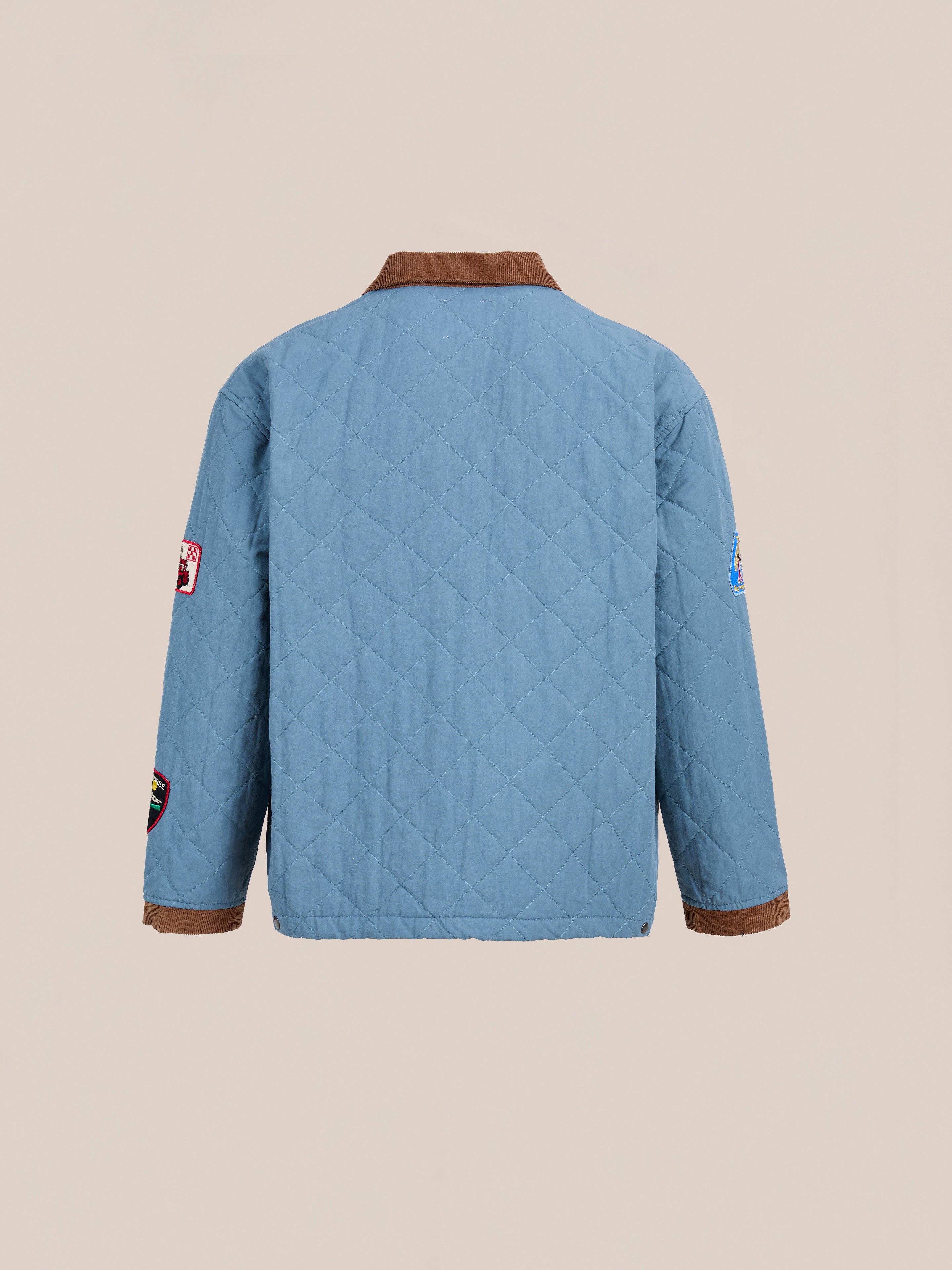 A light blue FOUND Farmstead Quilt Patch Jacket with a brown collar and cuffs, plus sleeve patches, is displayed from the back against a plain background.