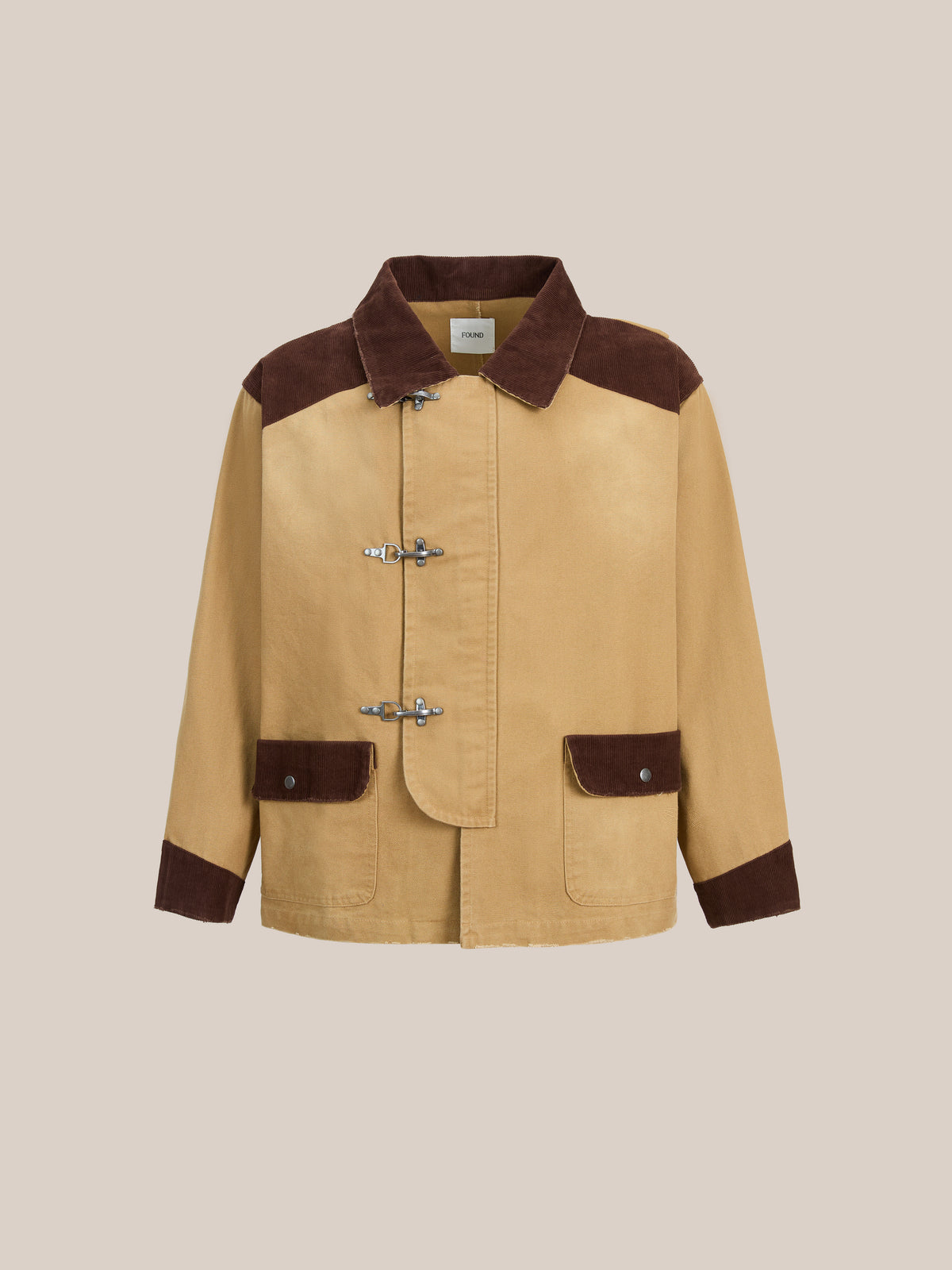 Introducing the Found Fireman Clasp Canvas Work Jacket: crafted from tan washed canvas with brown accents on the collar, cuffs, and pockets. This mid-weight, unisex jacket features four metal fireman clasp closures and two front pockets for everyday versatility. Shown against a plain beige backdrop, it offers a relaxed fit perfect for daily wear.