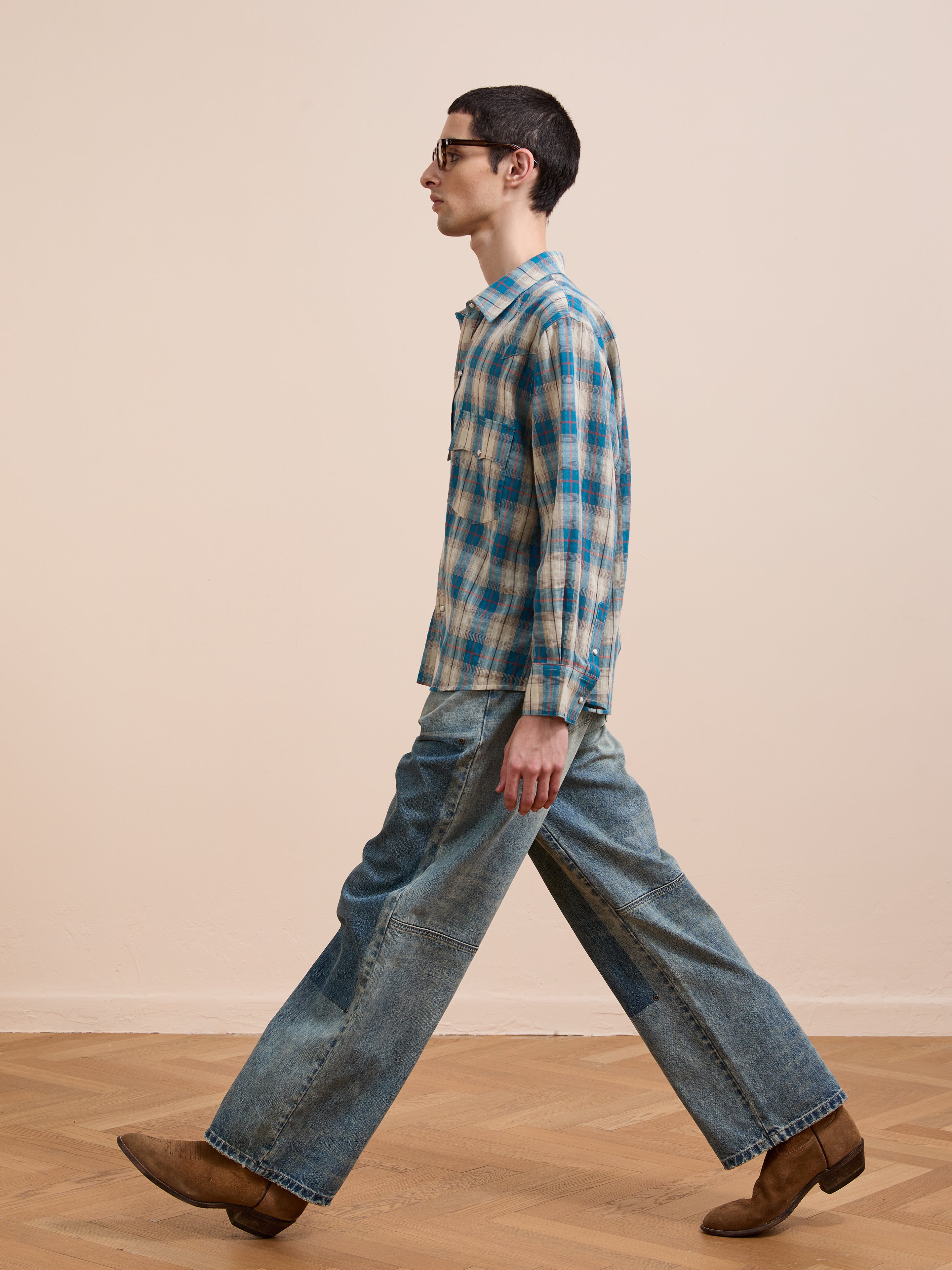 Someone wearing the FOUND Flannel Shirt, styled with wide-leg jeans and brown shoes, walks indoors on a wooden floor against a beige wall.