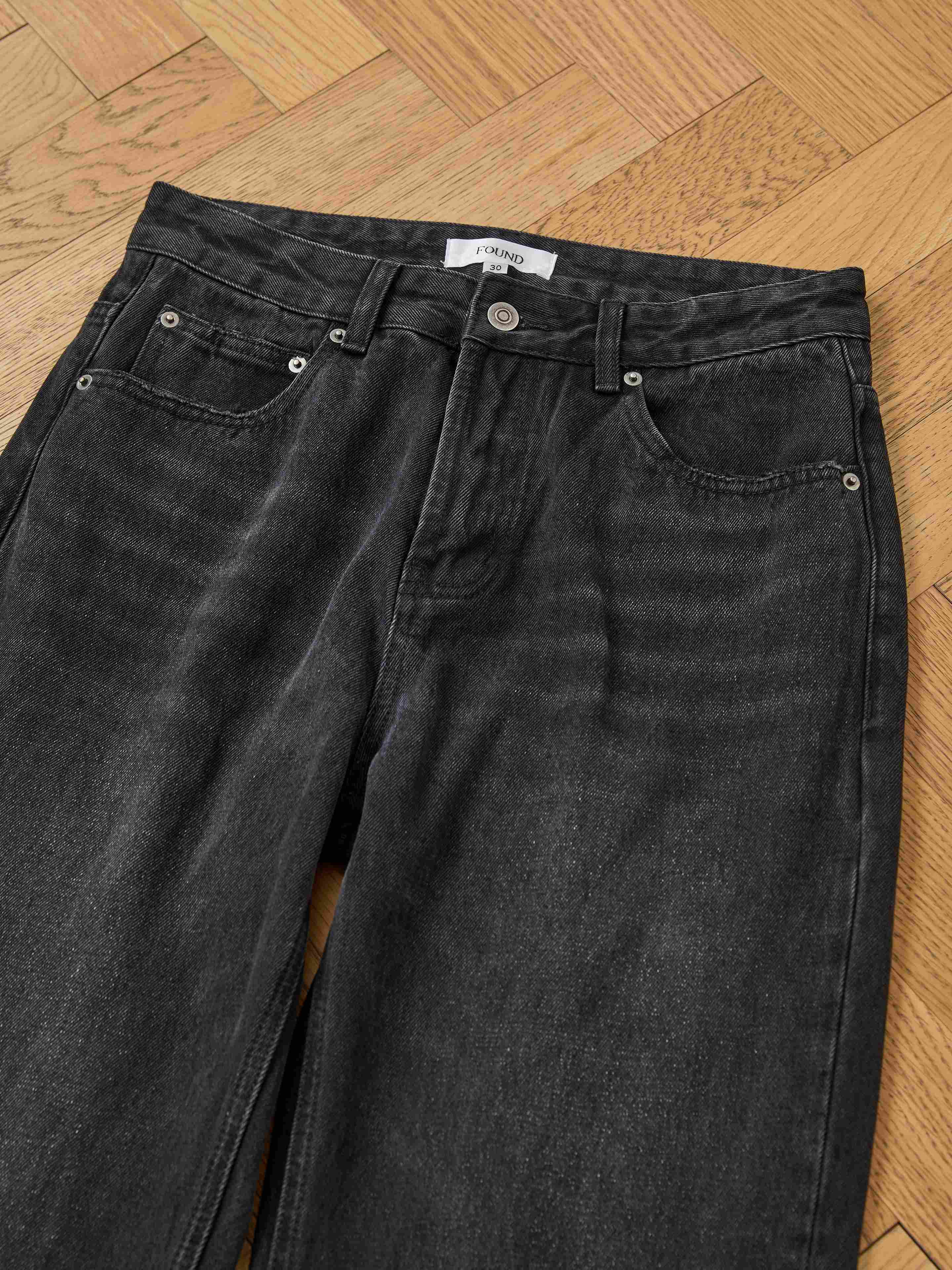 Found Flare Jeans in a vintage black wash, featuring front pockets and button closure, laid flat on a light wooden parquet floor.