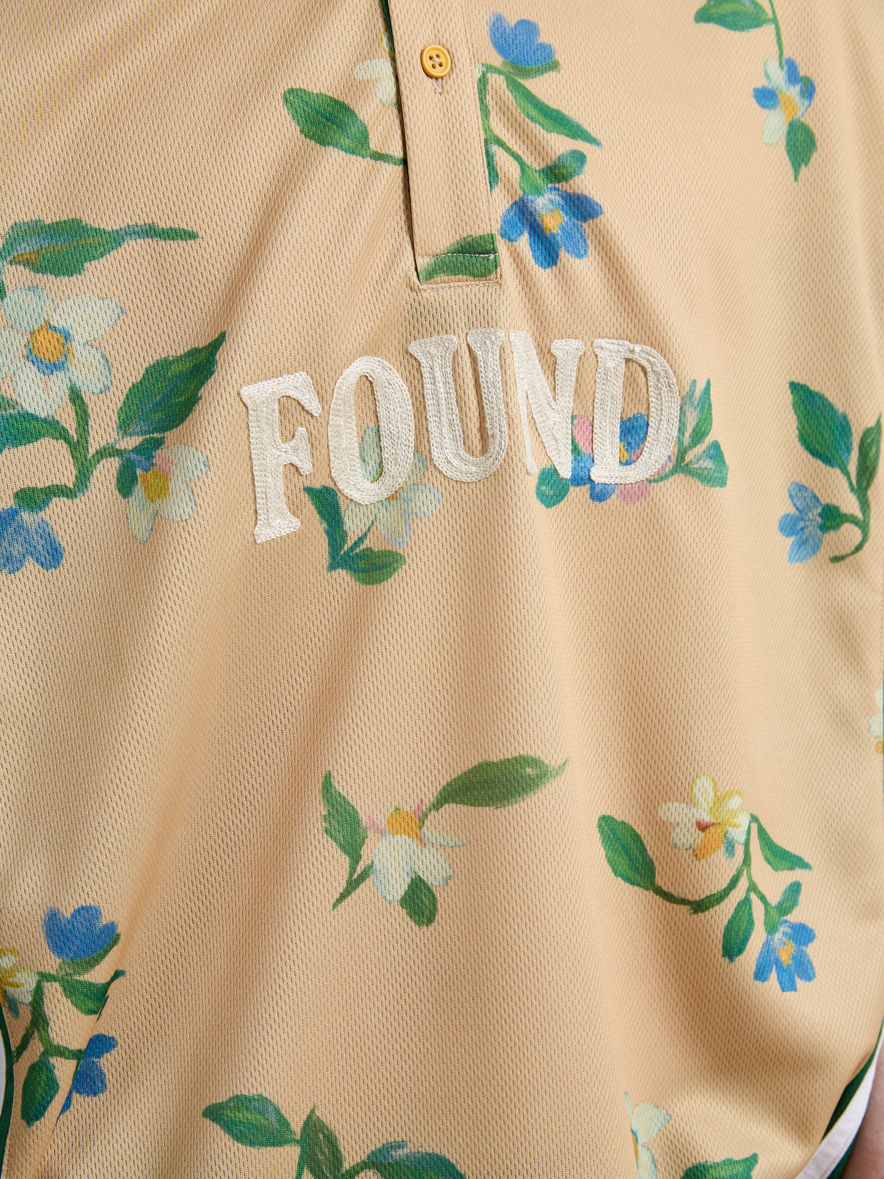 The FOUND Floral Polo Jersey is a beige unisex relaxed fit shirt with blue and white floral print, vintage sport-inspired, featuring "FOUND" embroidered in white on the front.