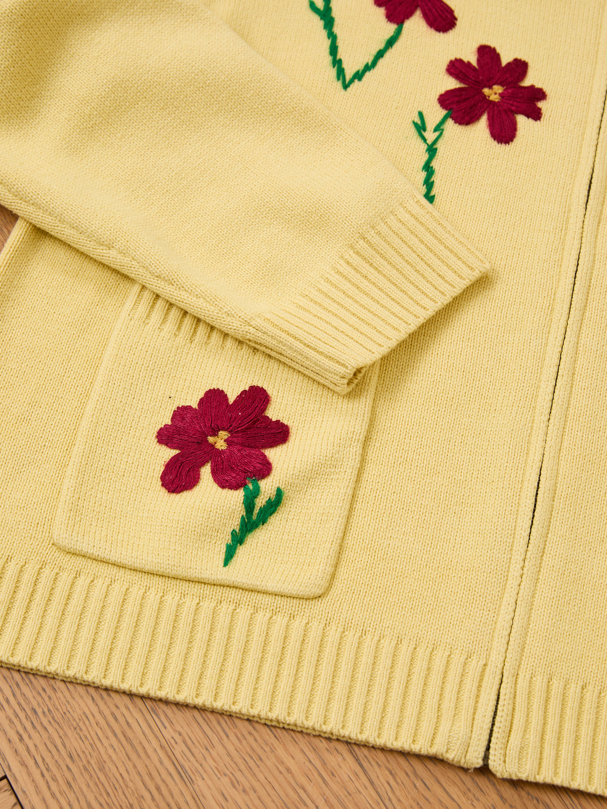 FOUND Floral Sun Knit Sweater—yellow vintage cardigan with red embroidered flowers, green stems; close-up of pocket, sleeve & hem on wood surface.
