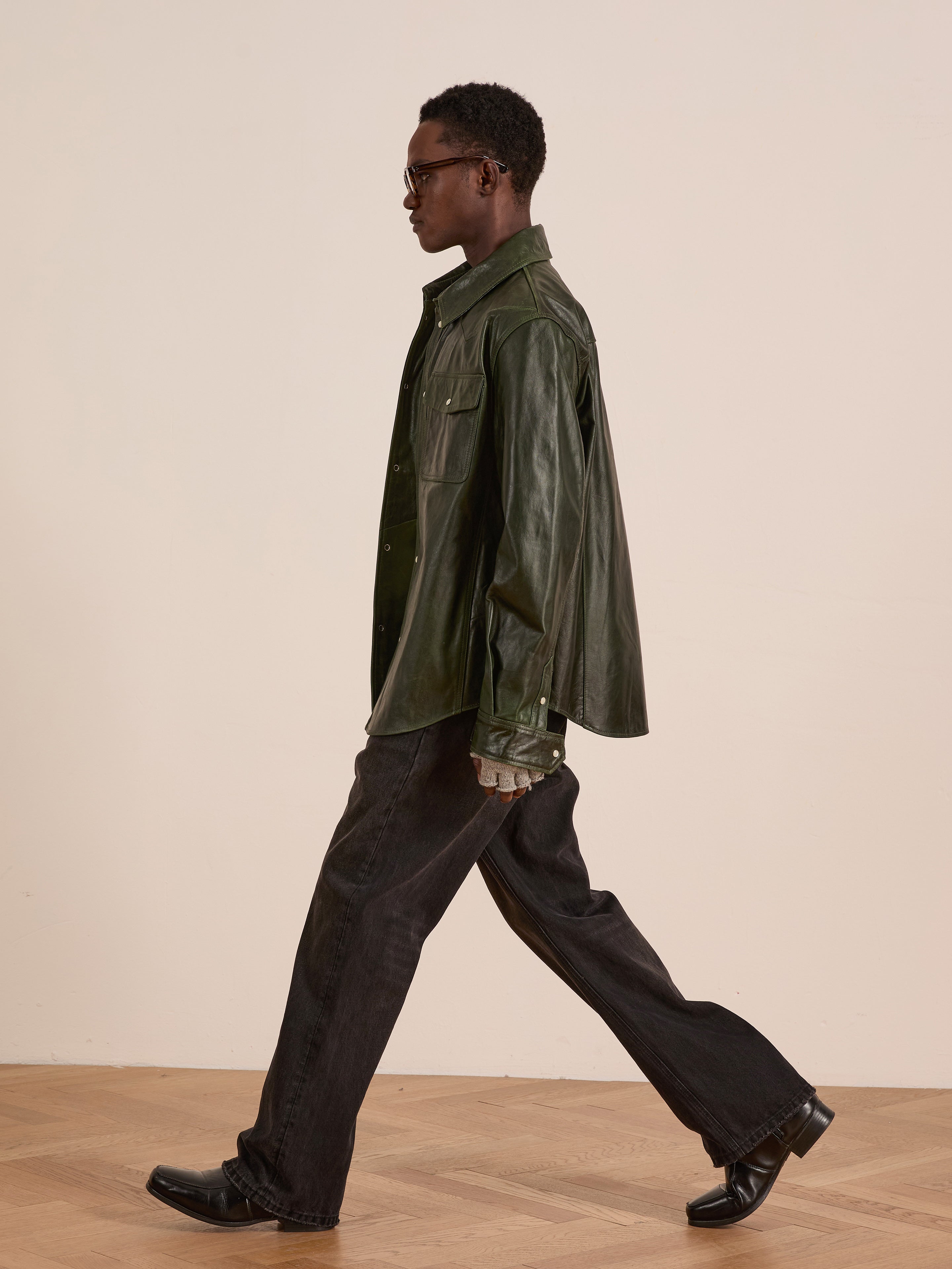 A person wearing the FOUND Forest Leather Western Shirt, paired with dark jeans and black shoes, walks across a wooden floor in front of a plain light-colored wall.