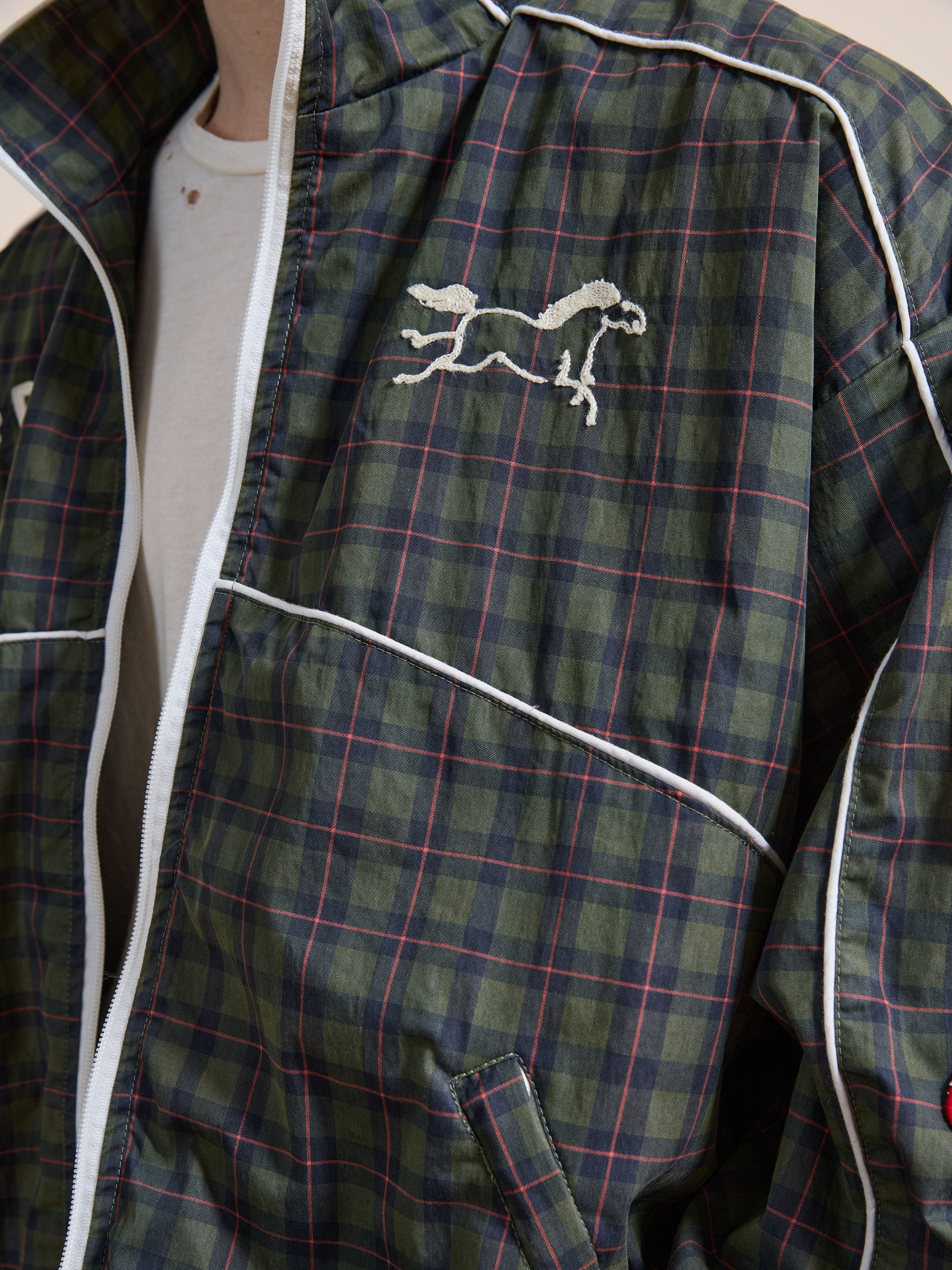 A person wears the FOUND Forest Plaid Track Jacket, featuring white piping and a horse emblem on the chest, layered over a crisp white t-shirt.