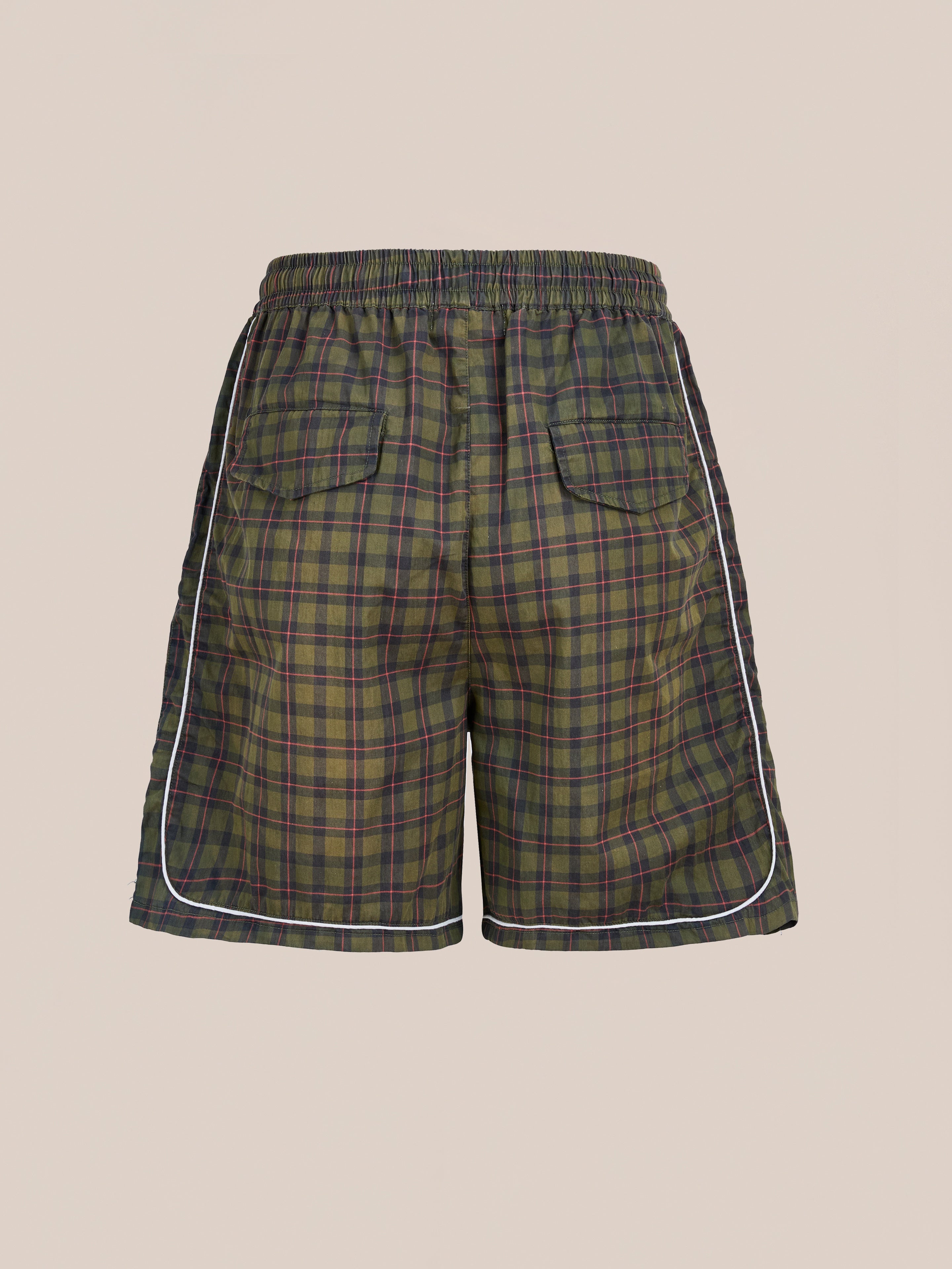 The Found Forest Plaid Track Shorts feature green and purple plaid, an elastic waistband, white side piping, and two back pockets in a unisex relaxed fit, shown against a plain beige background.