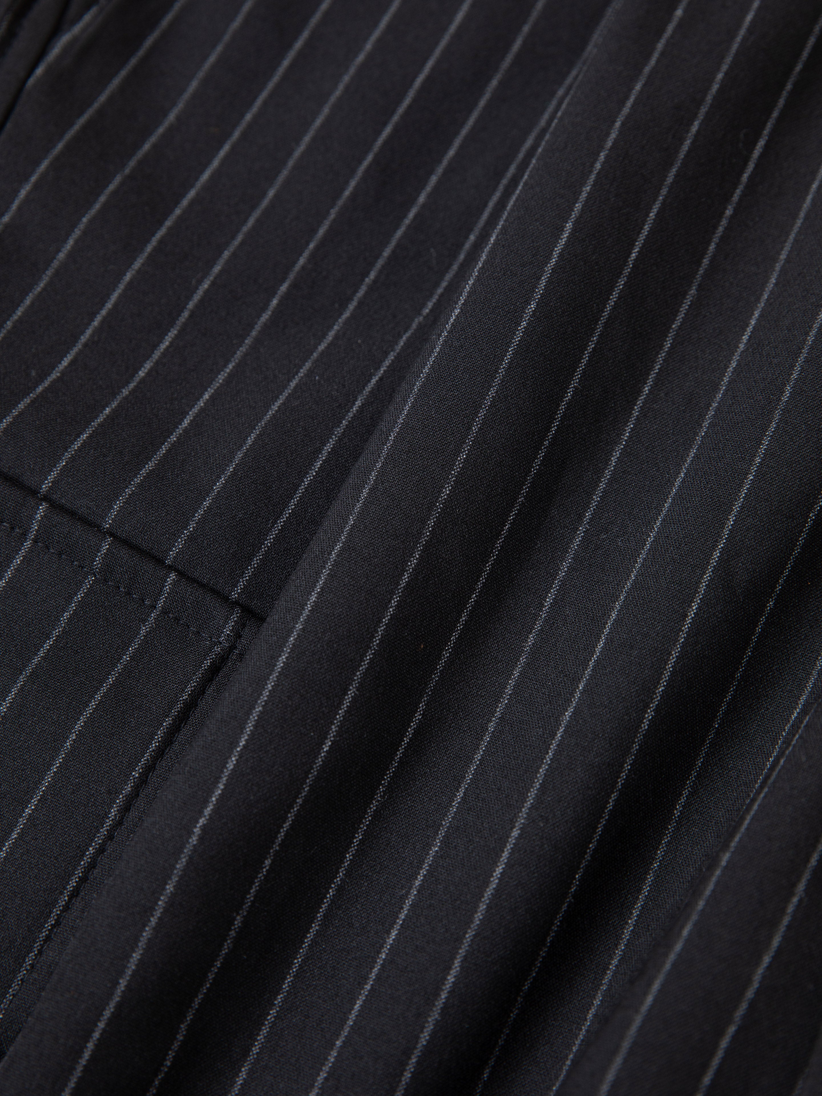 Close-up of black fabric with thin white pinstripes and a pocket, highlighting FOUND's Hava Pinstripe Pleated Cargo Trouser Shorts—stylish unisex design with an adjustable fit.