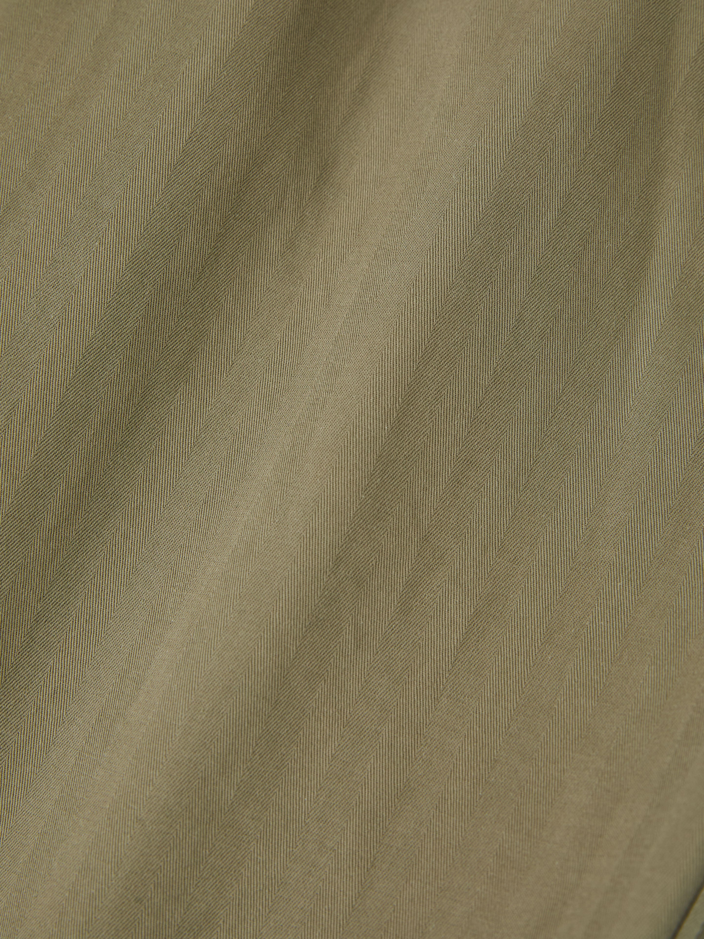 A close-up of a wool-blend fabric reveals a herringbone pattern in olive green, ideal for crafting stylish utility wear or versatile Hava Herringbone Pleated Cargo Trousers by FOUND.