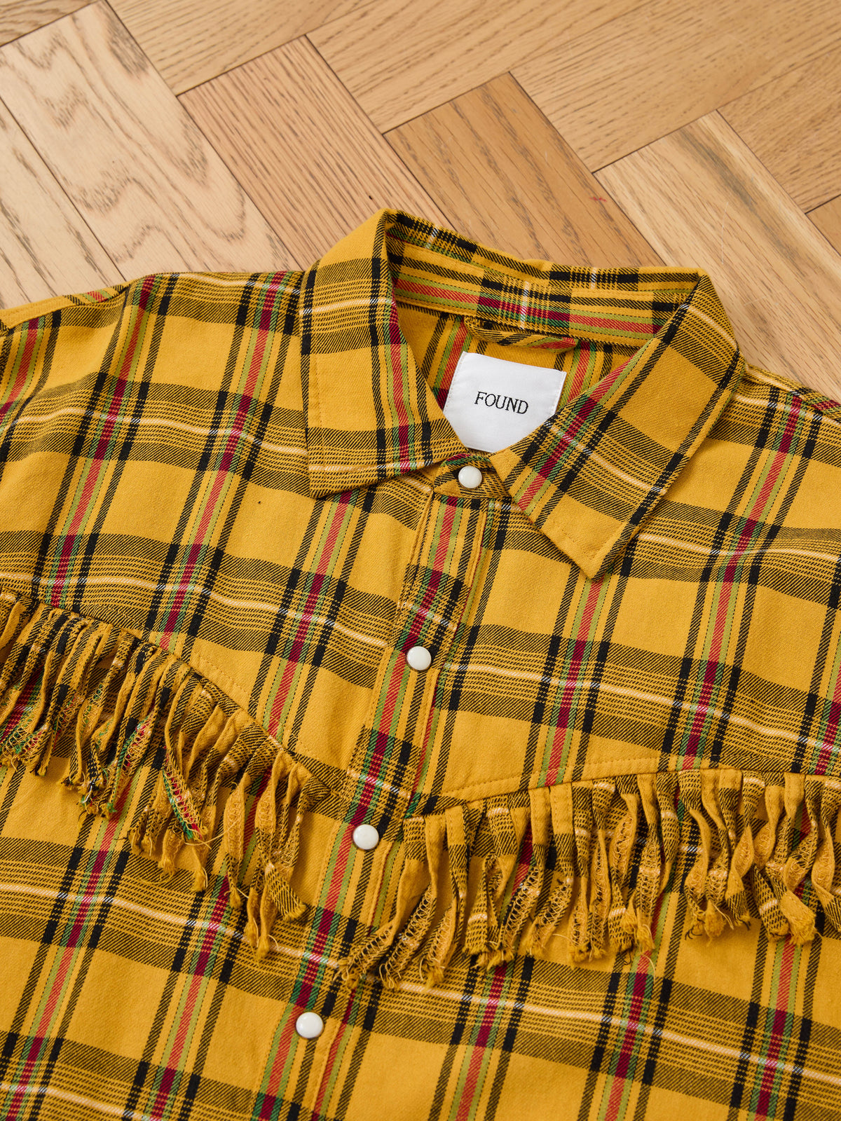 FOUND High Plains Fringe Shirt—yellow plaid with pearl snaps and distinctive chest fringe, shown on a wood parquet floor; a stylish unisex Western look.