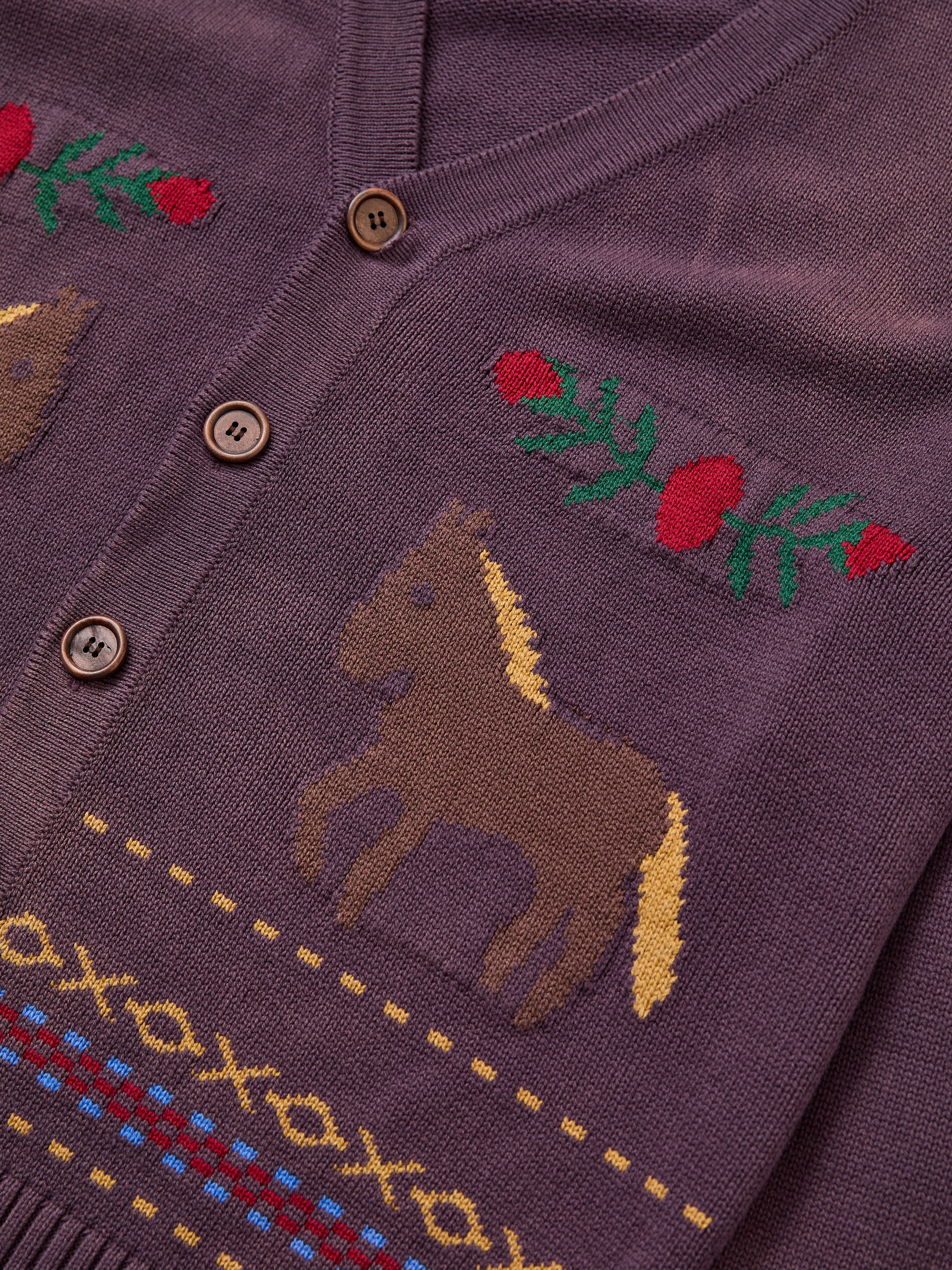 A close-up of the Found Horse Jacquard Cardigan, a unisex purple knit featuring brown buttons, horse motifs, and red floral embroidery.