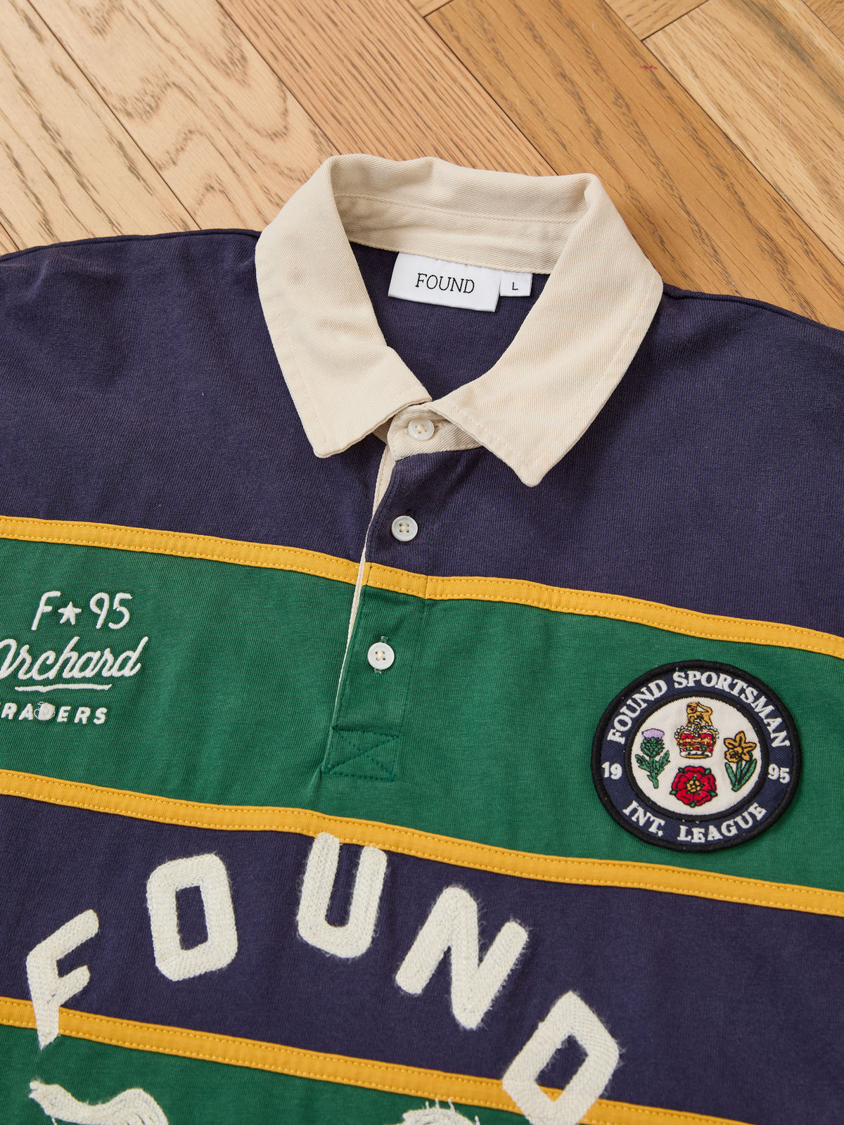 The FOUND Horse Logo Rugby is a vintage-style jersey with a beige collar, green and navy stripes, embroidered patches, and “FOUND” on the front.