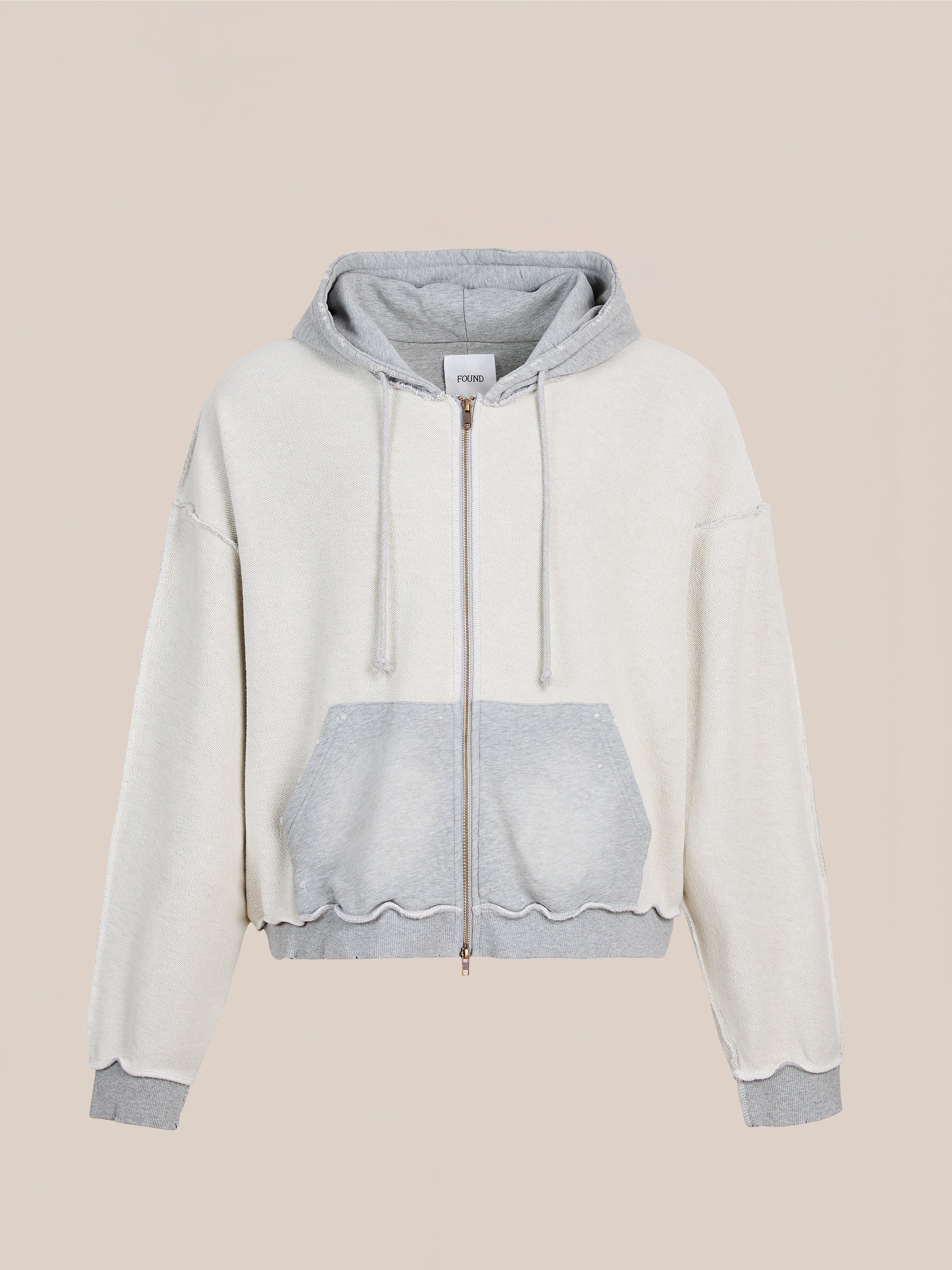 The FOUND Deconstructed Terry Zip Up Hoodie features a cream body with light gray hood, cuffs, hem, and front pocket in a unisex relaxed fit. Shown on a plain beige background.