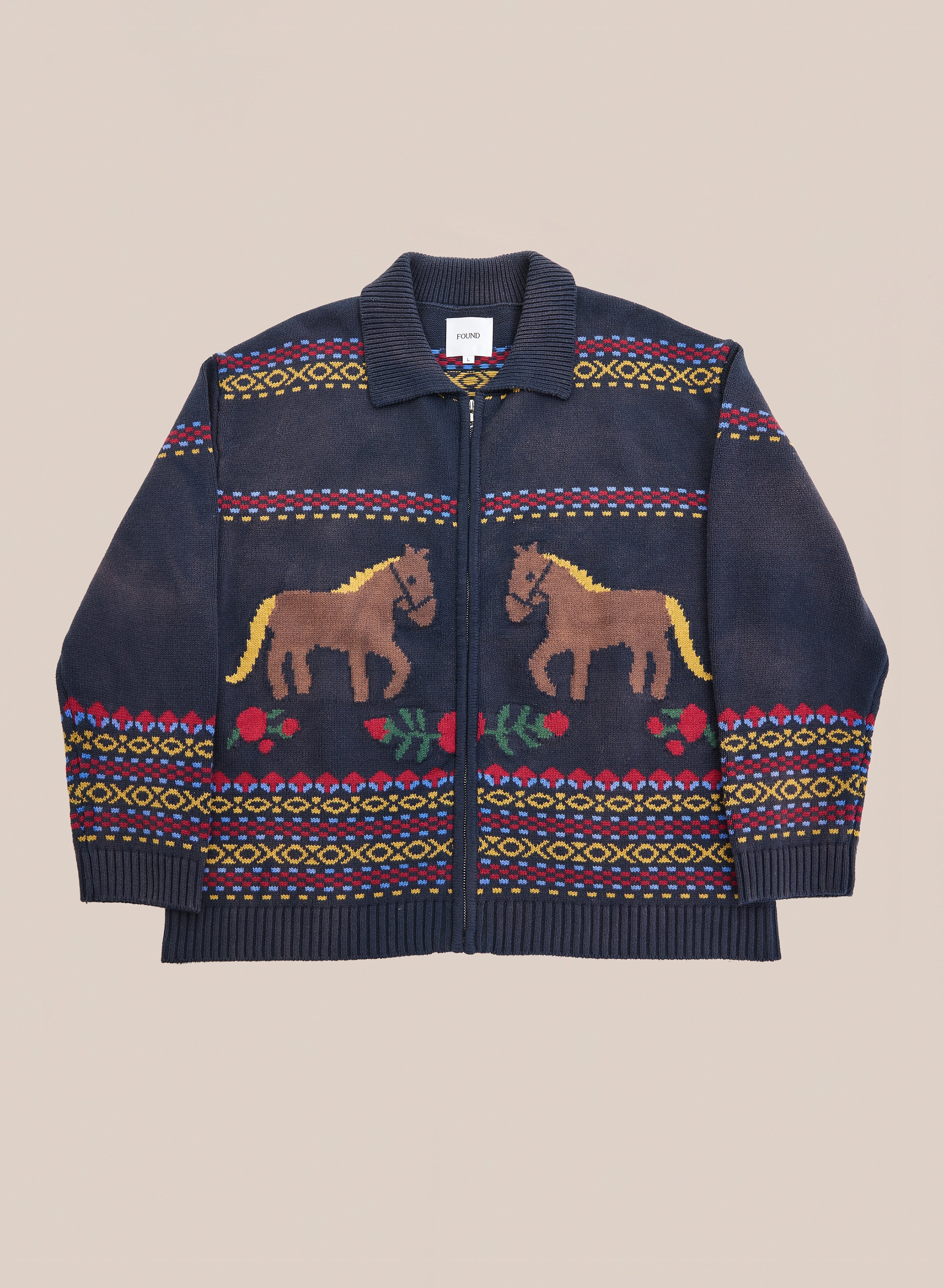Introducing the Isles Sweater by Found: a navy blue knit zip cardigan featuring brown jacquard horse motifs, red floral patterns, and bold geometric designs on the sleeves and hem, finished with a ribbed collar and zip front.
