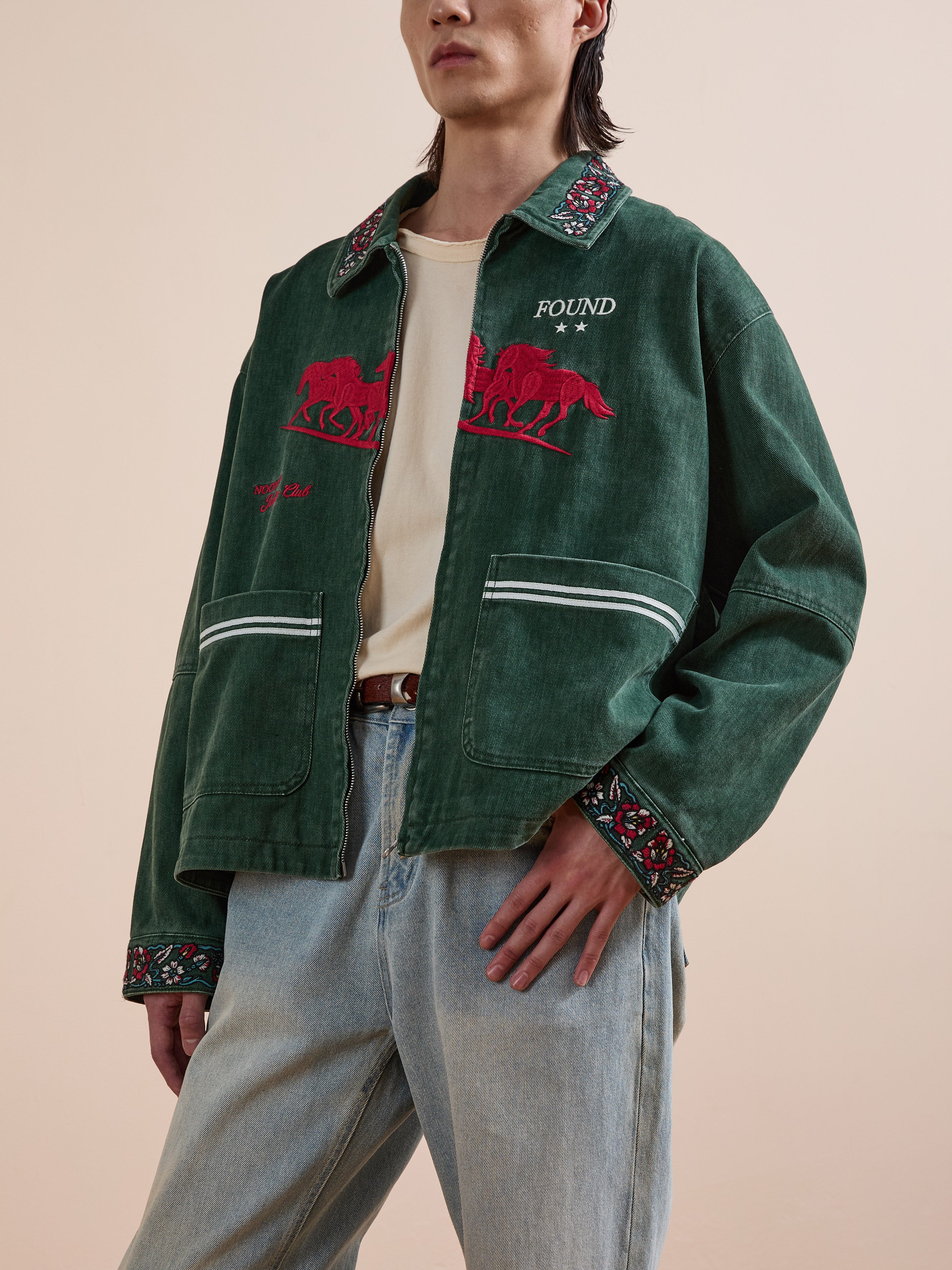 A person wears a Found Jockey Club Embroidered Jacket with racing horses, patterned collar and cuffs, a beige shirt, and light blue unisex relaxed fit jeans.