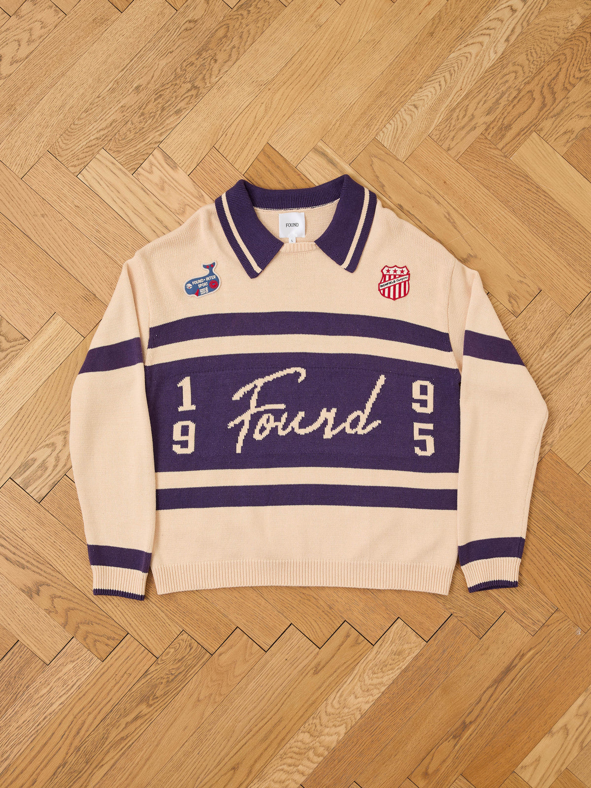 FOUND Knit Jersey in beige and purple with “1995 Found” text and two chest patches, long-sleeve collared style, displayed on herringbone wood floor.