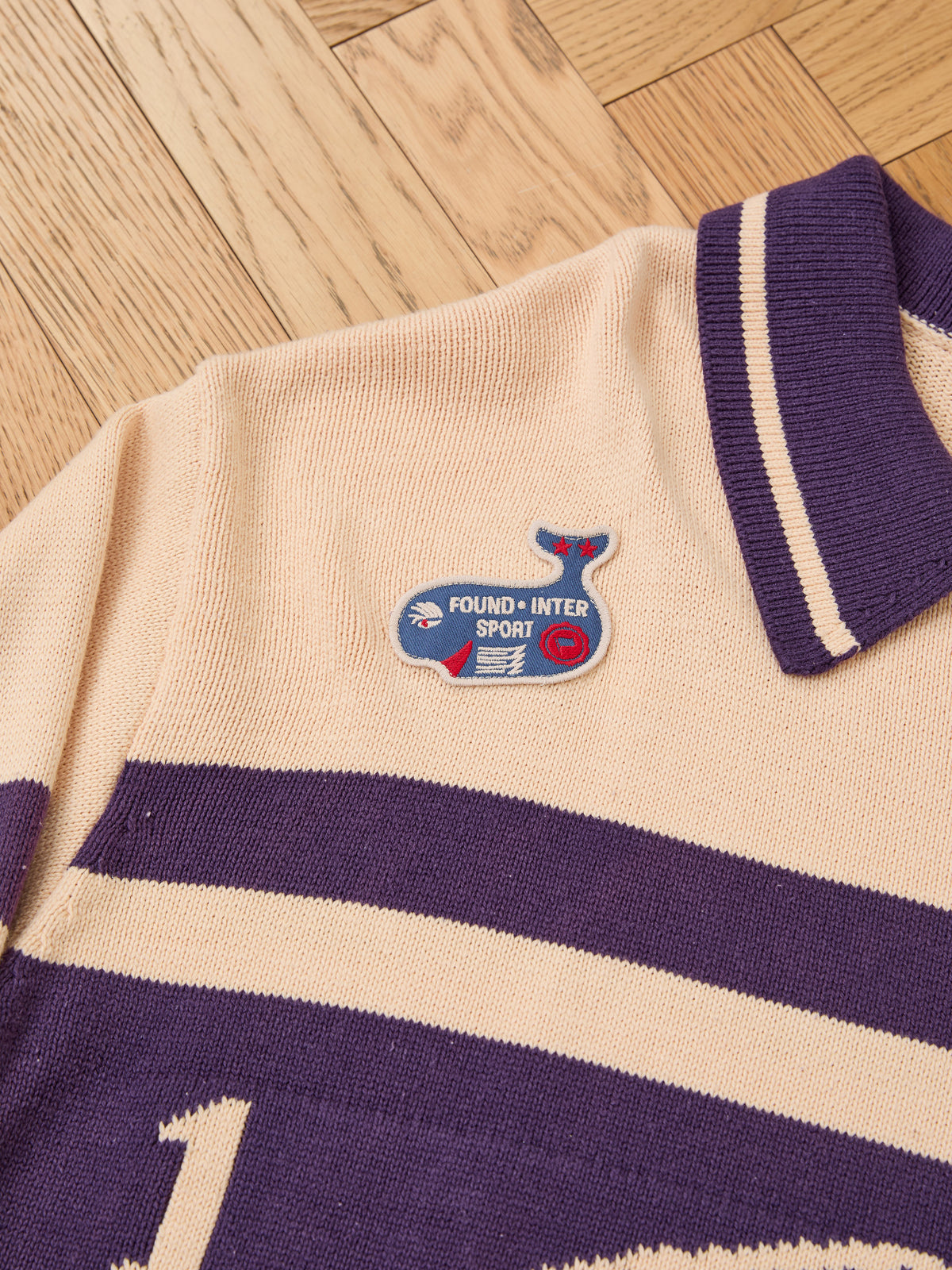 Beige and purple FOUND Knit Jersey with a collared design and whale patch, vintage club sweater vibes, displayed on a wooden floor.