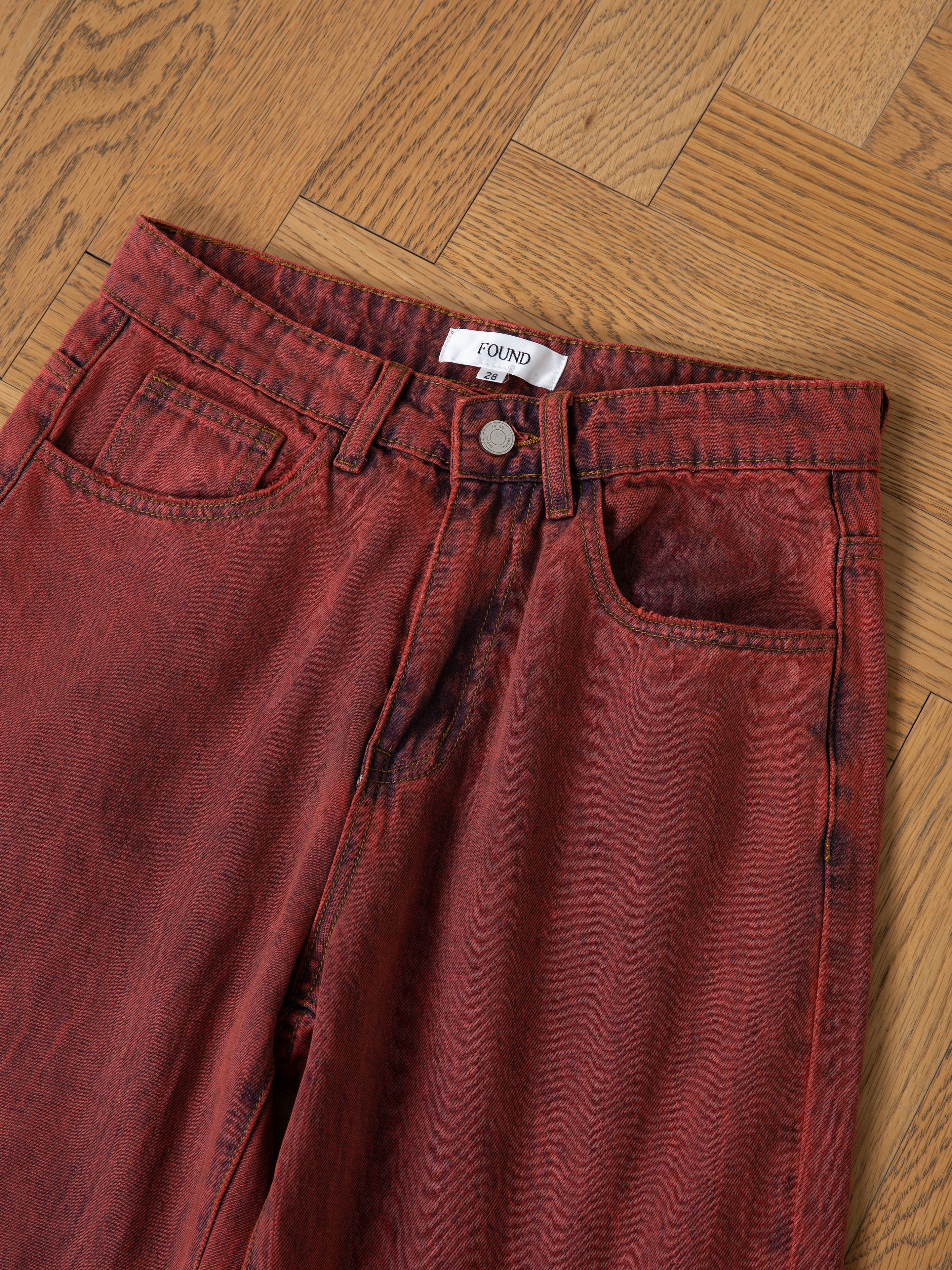 A pair of FOUND Lacy Jean Jorts in red acid wash, shown on a light wood parquet floor—ideal for making a bold unisex fashion statement.