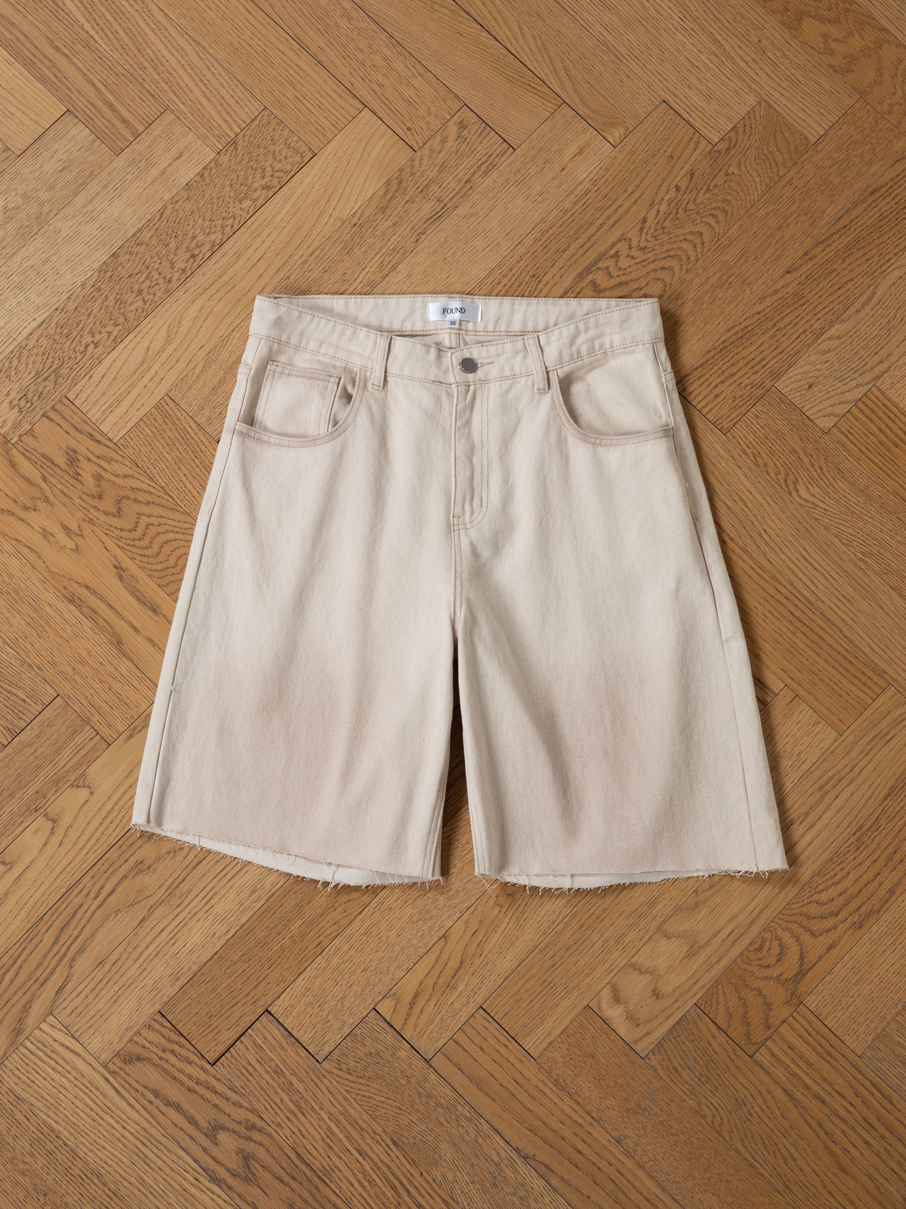 FOUND Lacy Jean Jorts in beige, relaxed fit with frayed hems and five pockets, shown laid flat on a wooden herringbone floor.