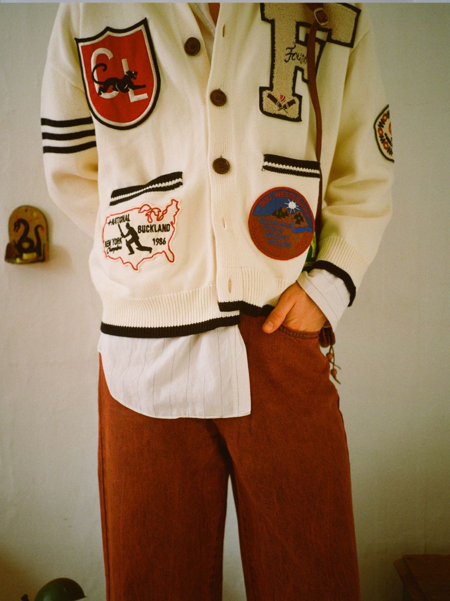 A person wearing a white cardigan with patches and FOUND's Lacy Baggy Jeans stands against a plain background, showcasing a unisex style.