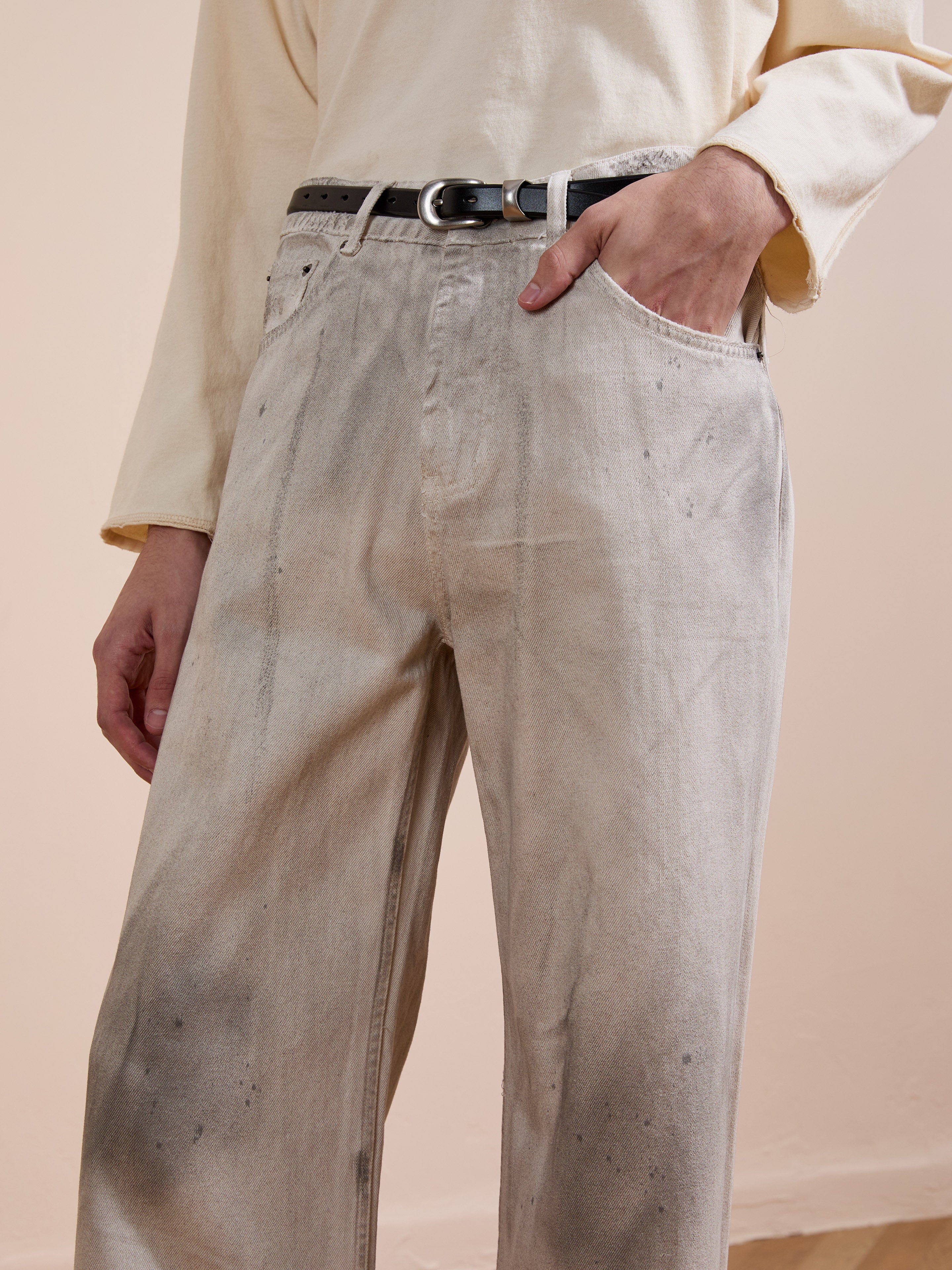 A person wears a light long-sleeve shirt, a black belt, and FOUND Lacy Baggy Jeans in a distressed concrete wash, with one hand casually tucked in their pocket.