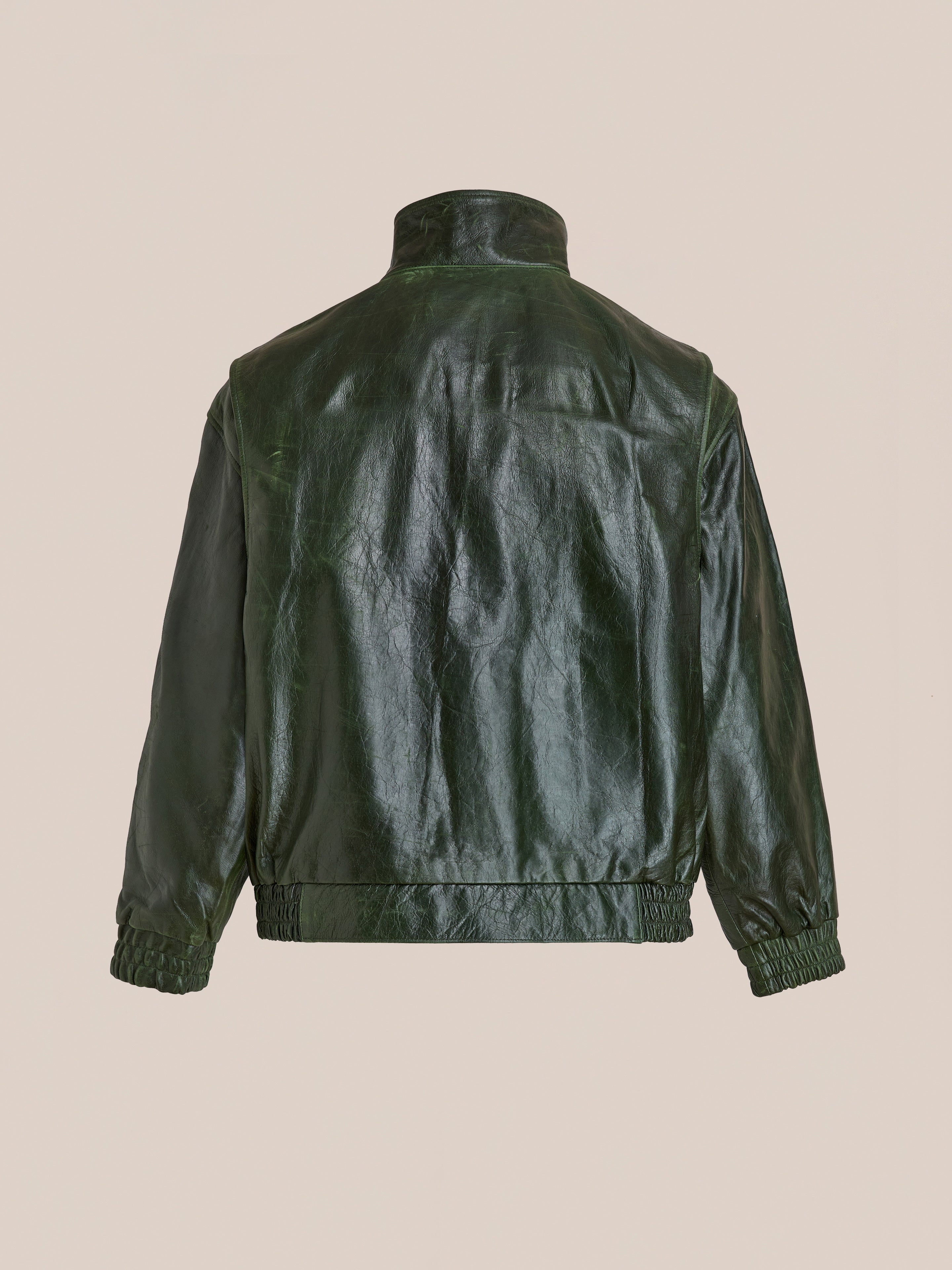 FOUND’s Forest Leather Bomber Jacket in dark green genuine leather, shown from the back with a stand collar, elastic cuffs, and waistband, set against a plain beige background.