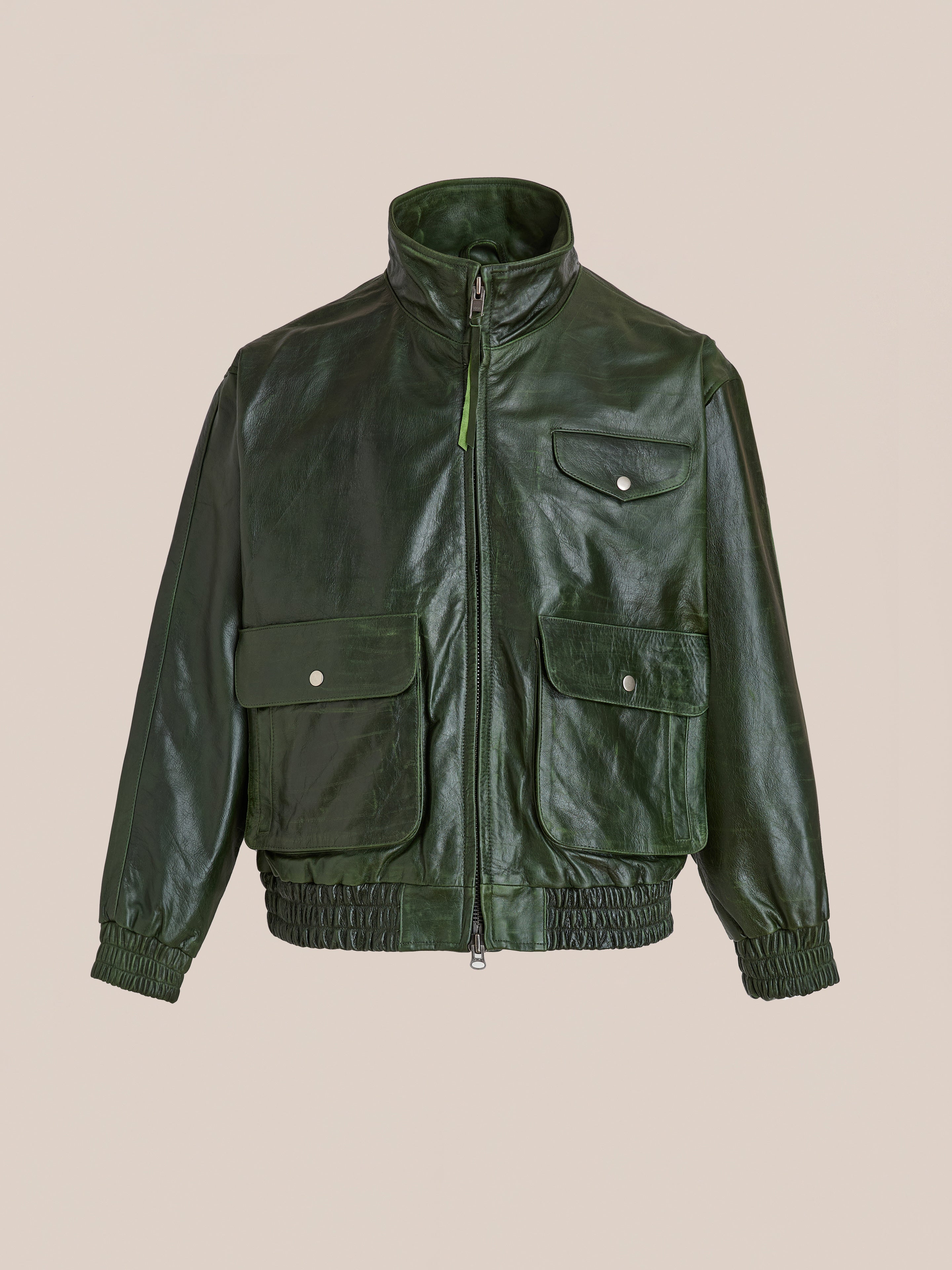 The FOUND Forest Leather Bomber Jacket features dark green genuine leather, a front zipper, high collar, chest and front flap pockets, plus elasticized cuffs and hem. This unisex style combines durability and modern appeal.