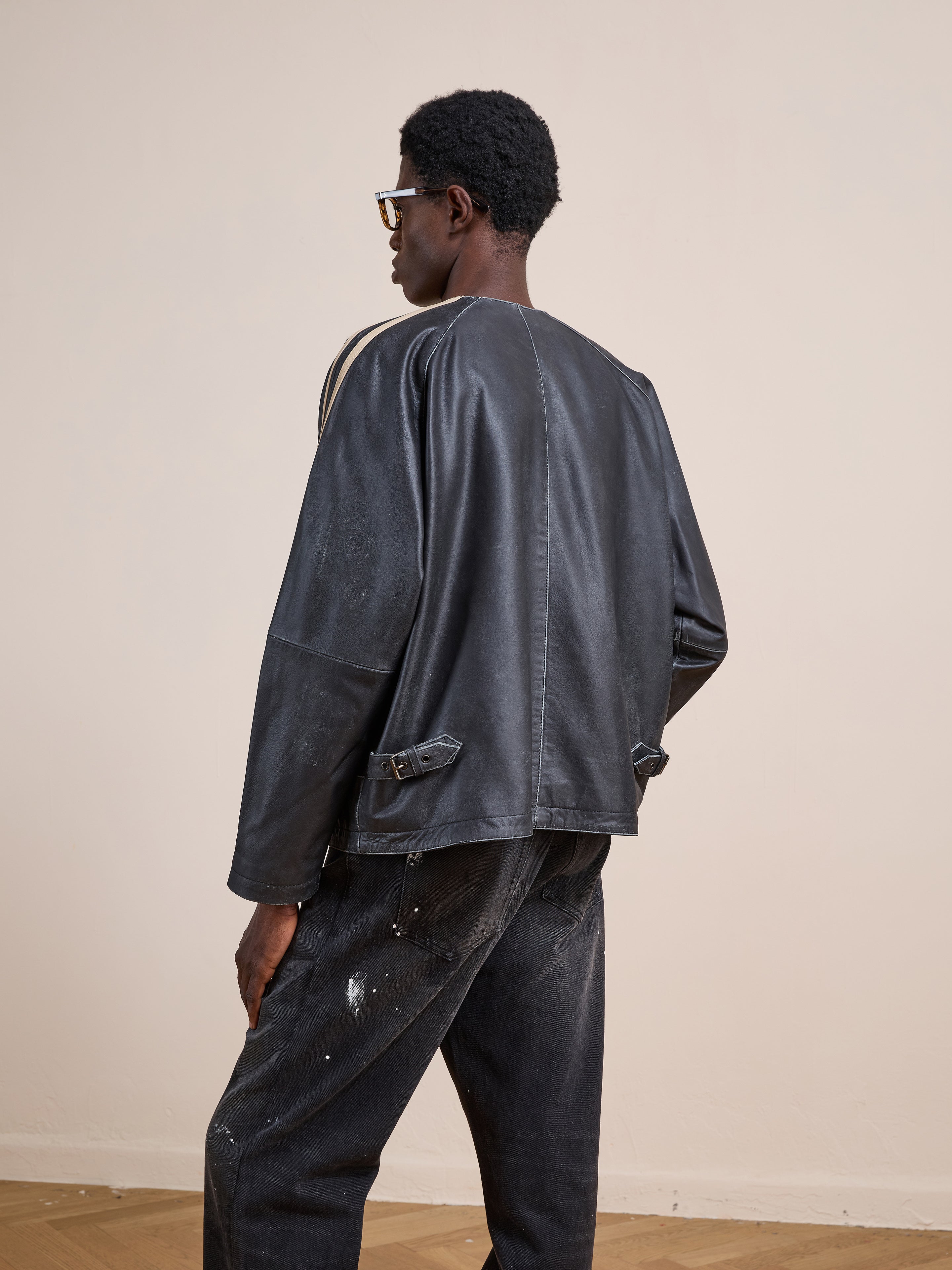 A person models the FOUND Leather Track Jacket with black jeans, standing sideways and facing away from the camera against a plain beige background.