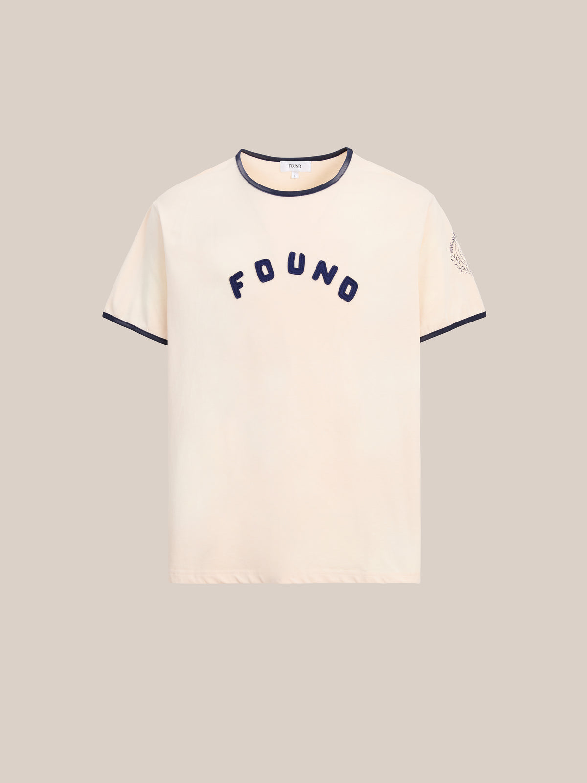 FOUND’s Logo Felt Patch Ringer Tee in beige features short sleeves, contrasting black trim, and “FOUND” embroidered across the chest. A felt patch accents the left sleeve. This unisex tee offers a relaxed fit for effortless, everyday style.
