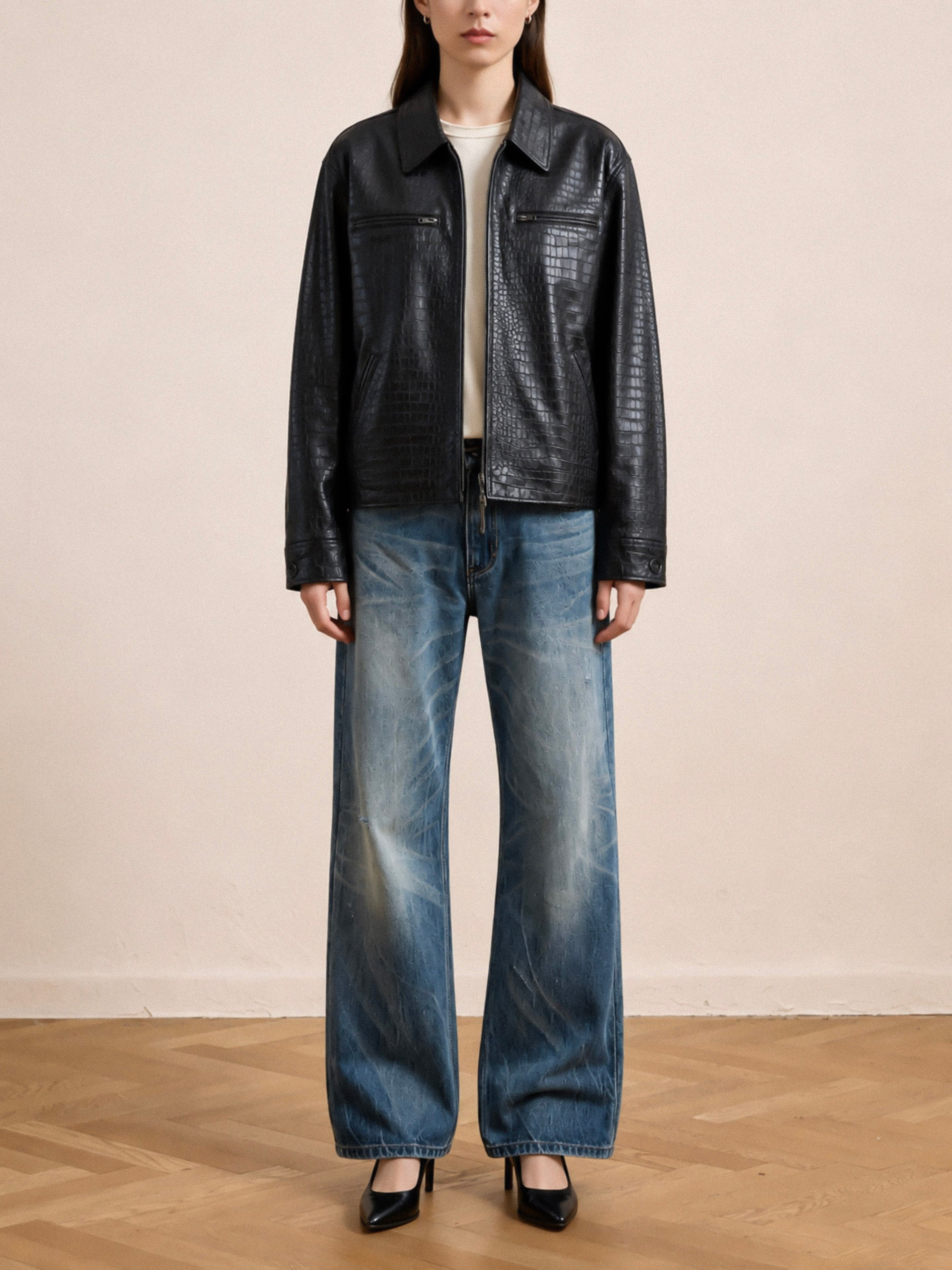Wearing the FOUND Marlboro Croc Embossed Leather Racer Jacket—handmade in Pakistan and featuring a unisex relaxed fit—paired with a white shirt, wide-leg blue jeans, and black heels, the person stands on a wooden floor against a plain light-colored wall. The modern edge of the jacket elevates the ensemble.