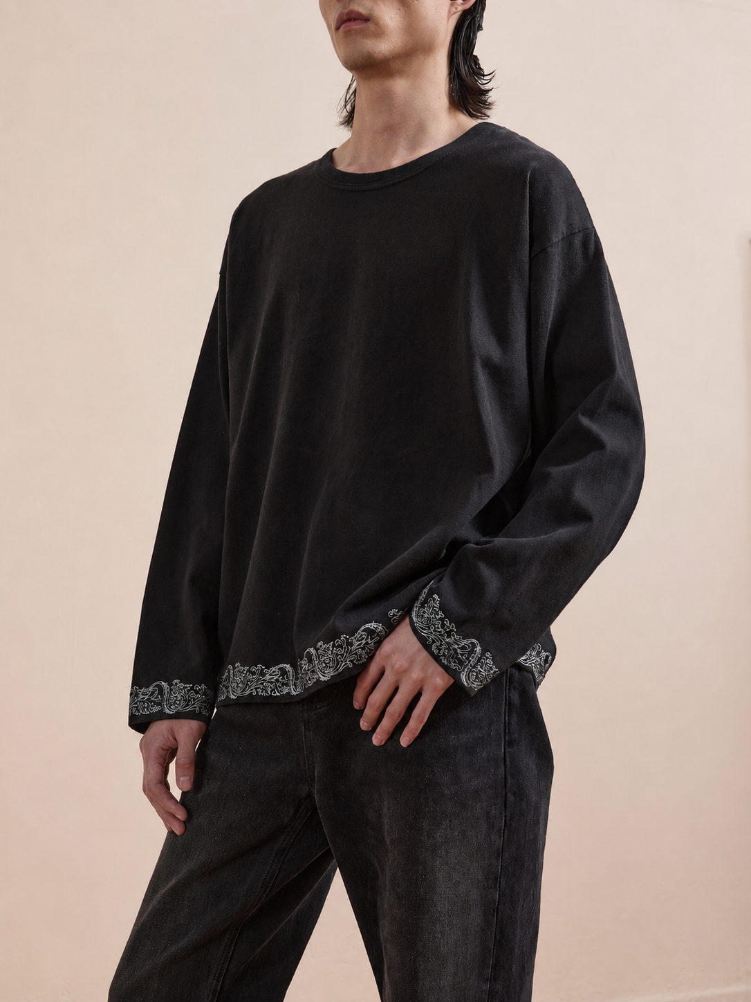A person in the FOUND Metallic Long Sleeve Embroidered Tee and unisex relaxed fit black jeans stands against a plain background.