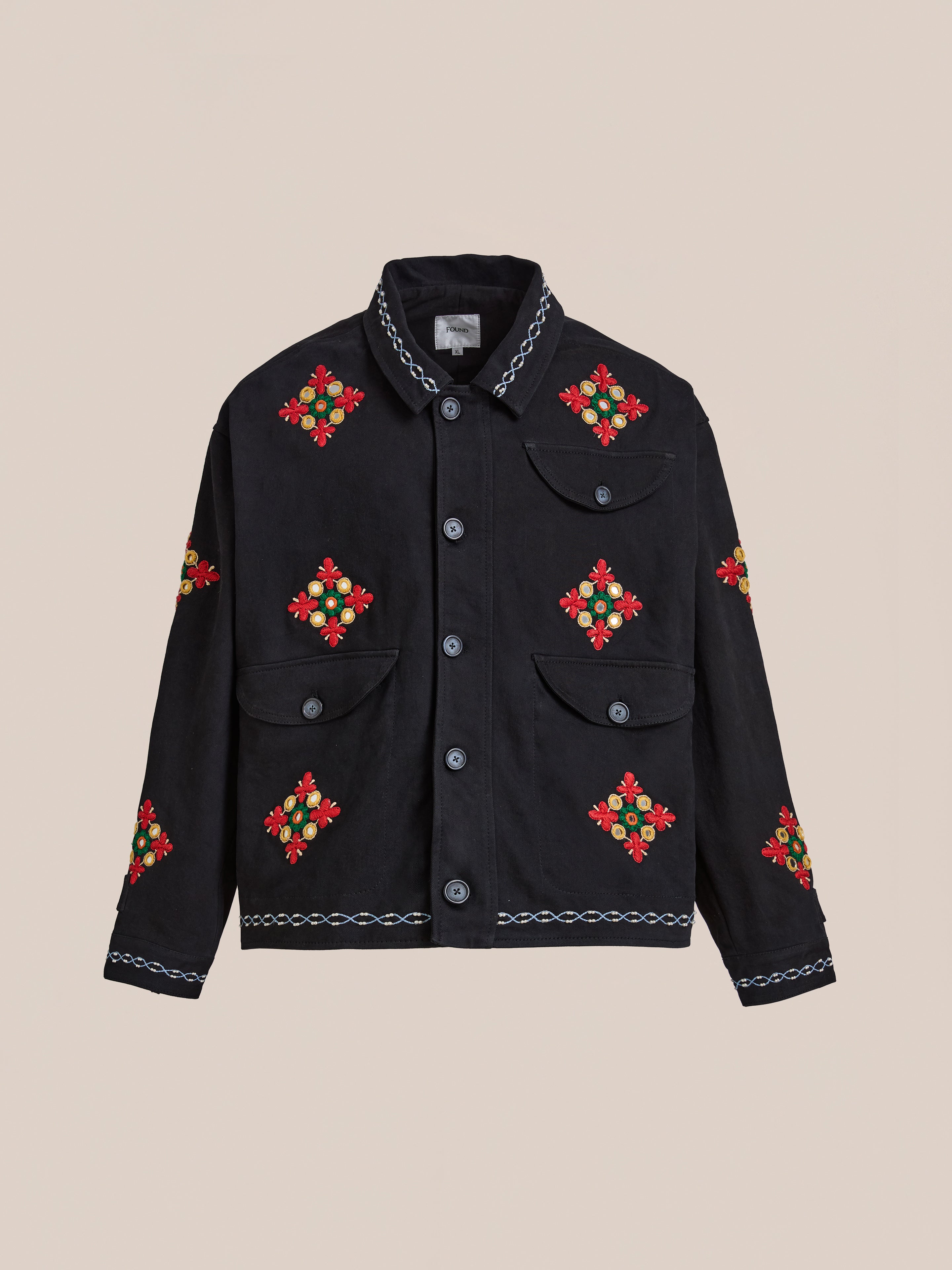 The Mirror Ornament Hand Embroidered Work Jacket by Found features striking red, yellow, and green floral designs on black cotton with Aari embroidery, displayed on a beige background—an eye-catching piece to elevate any look.