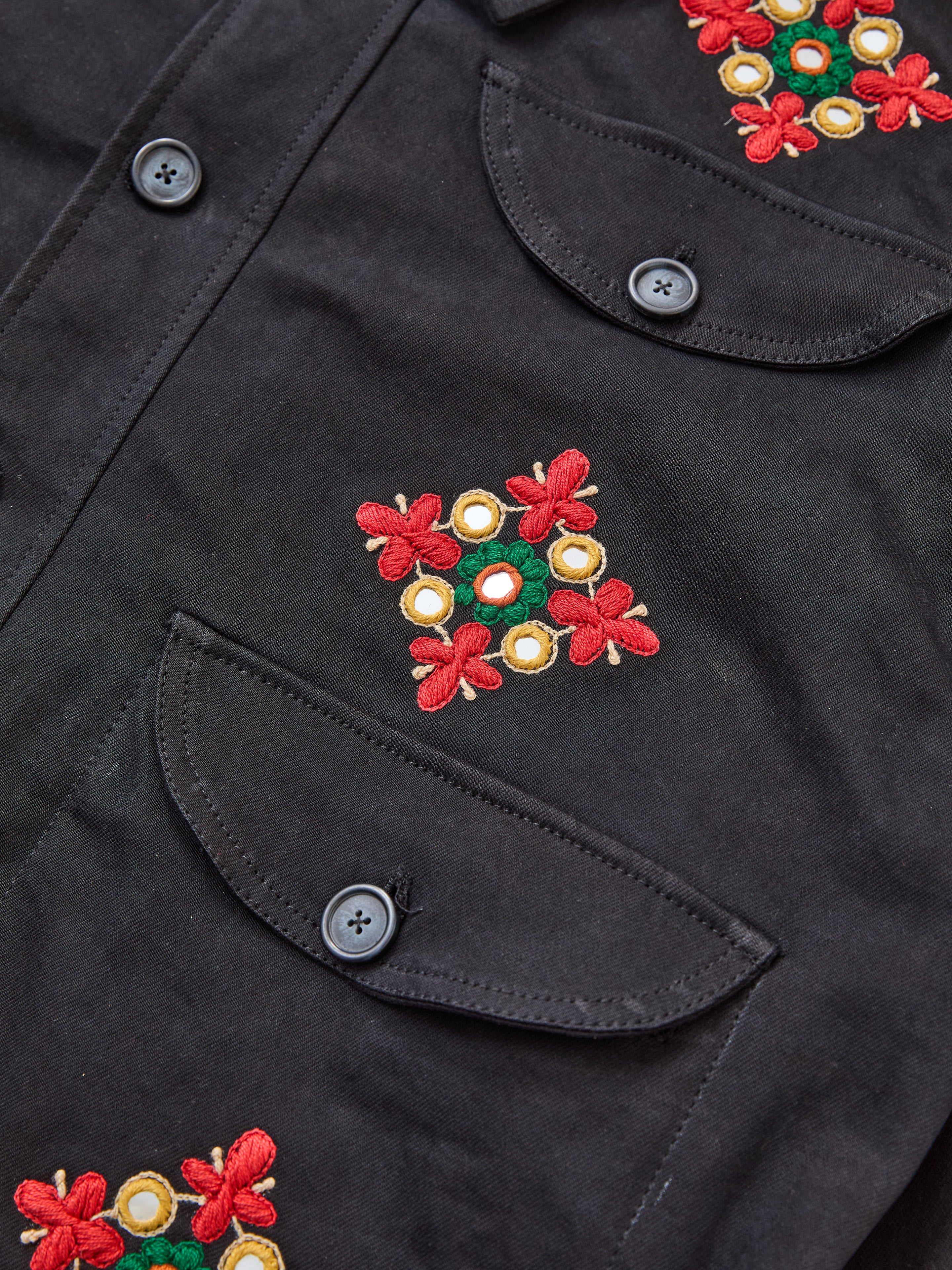 Close-up of the Mirror Ornament Hand Embroidered Work Jacket by Found, crafted from cotton with front pockets, black buttons, and vibrant red, yellow, and green floral embroidery.
