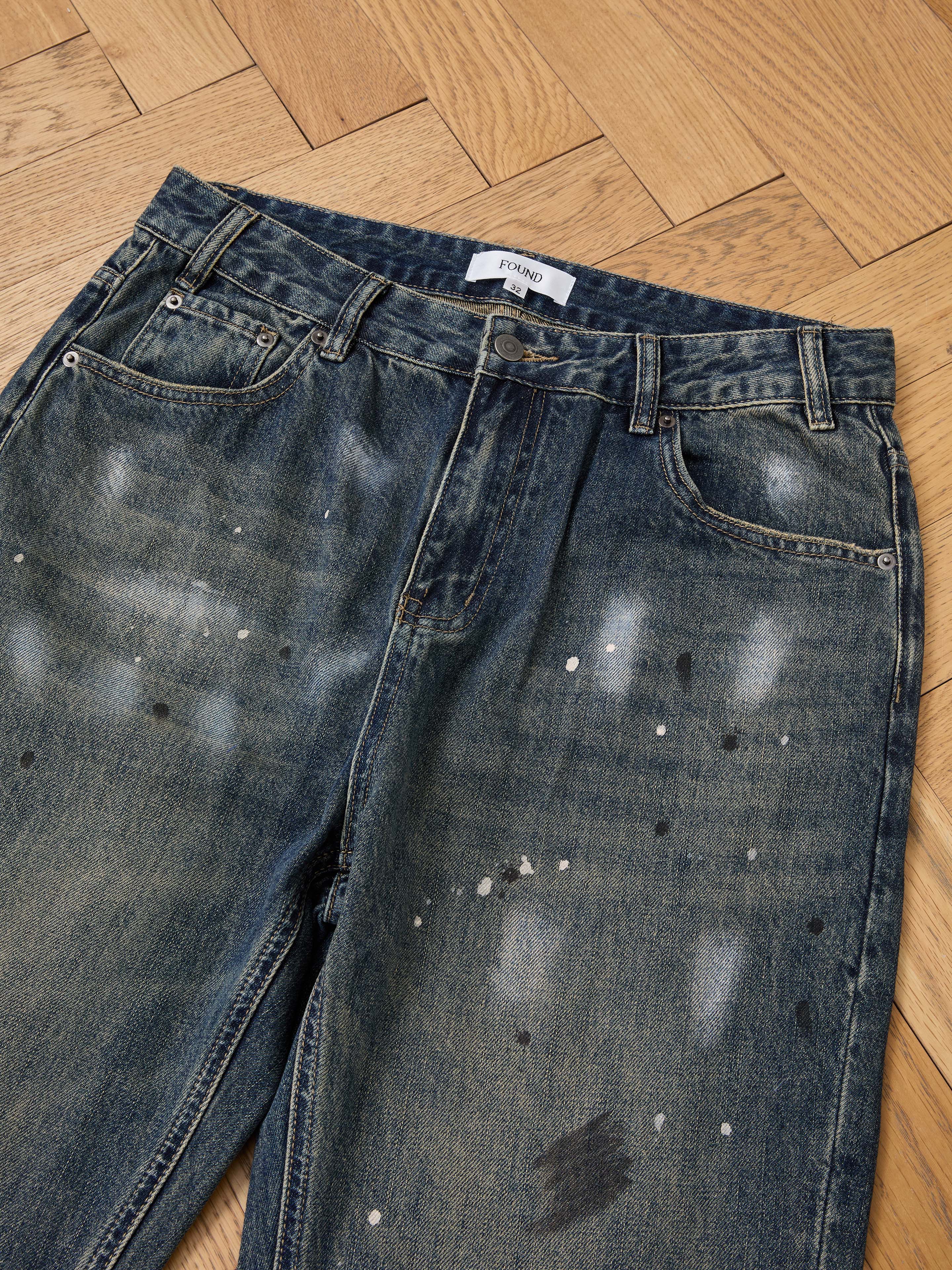 FOUND Monet Paint Jeans in vintage blue with paint splatters and a distressed look, shown laid flat on wood. Unisex relaxed fit for easy style.