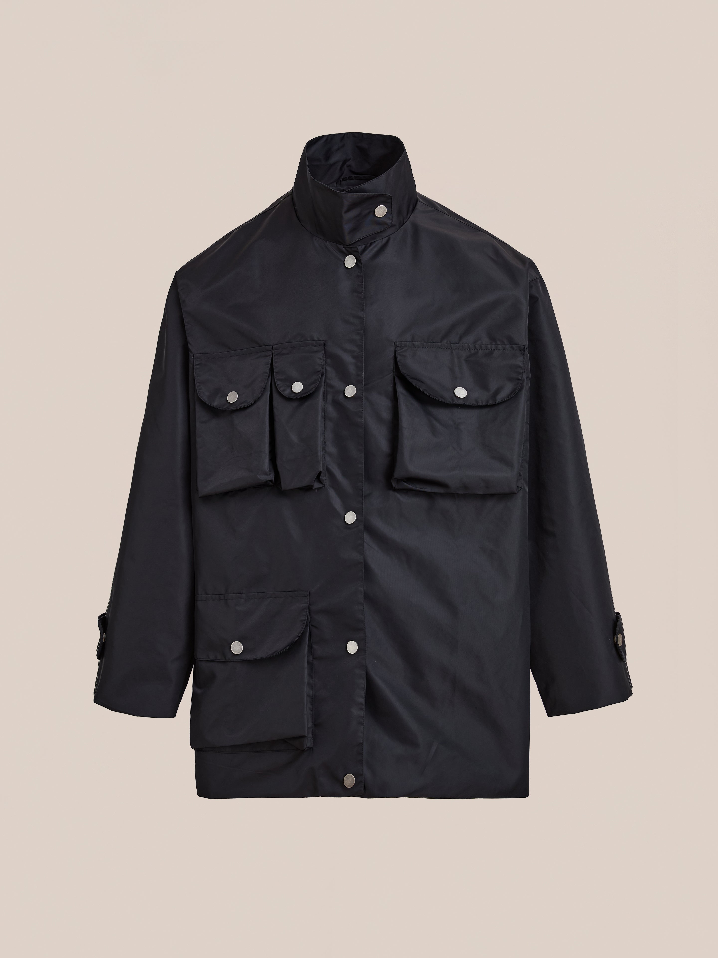 The FOUND Cargo Nylon Jacket is a black unisex design with long sleeves, a high collar, and multiple front flap pockets, shown against a plain beige background.