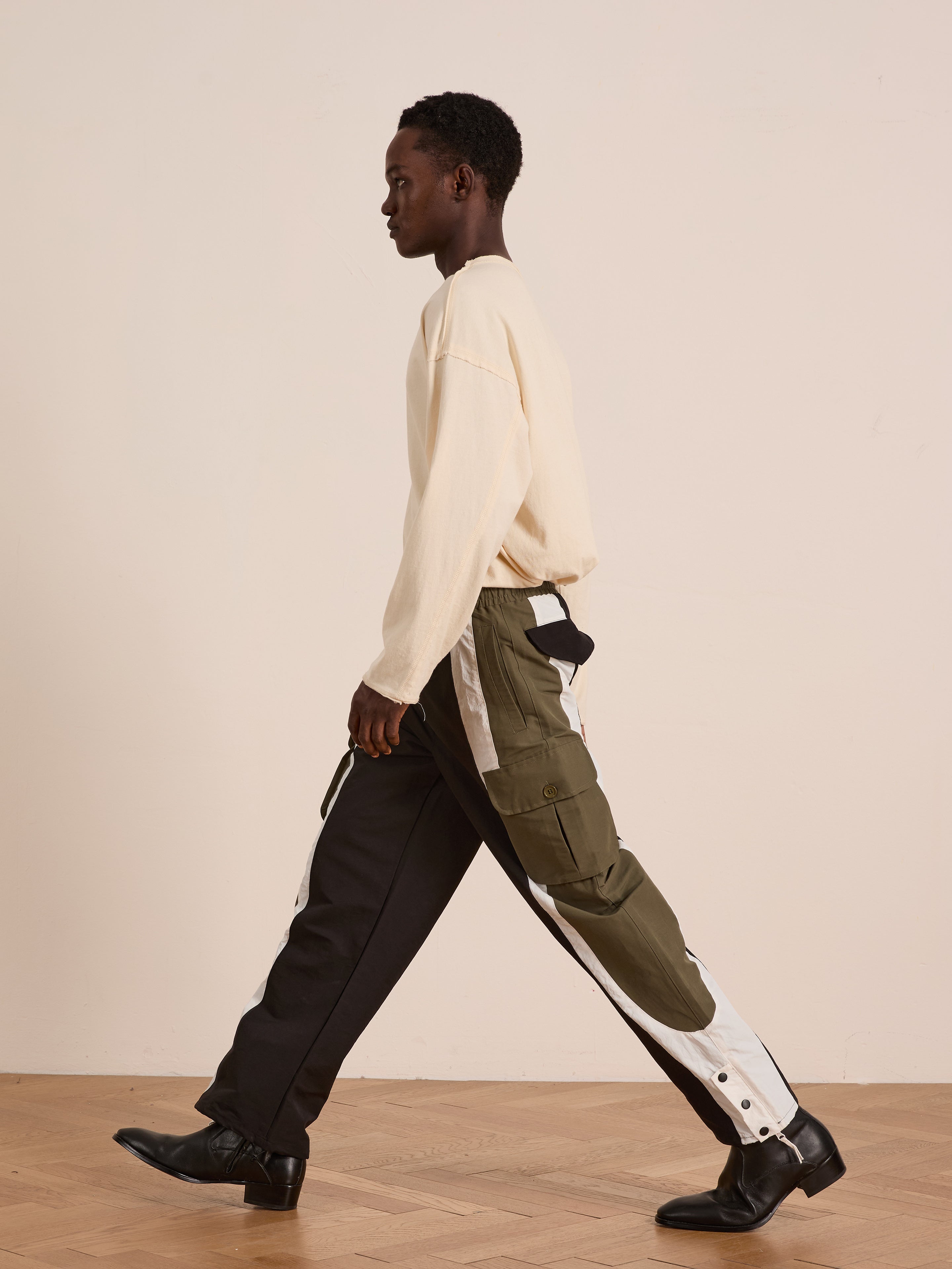 A person in a cream long-sleeve shirt and Found Sporting Club Track Pants with an adjustable waistband walks indoors on a wooden floor against a plain light wall.